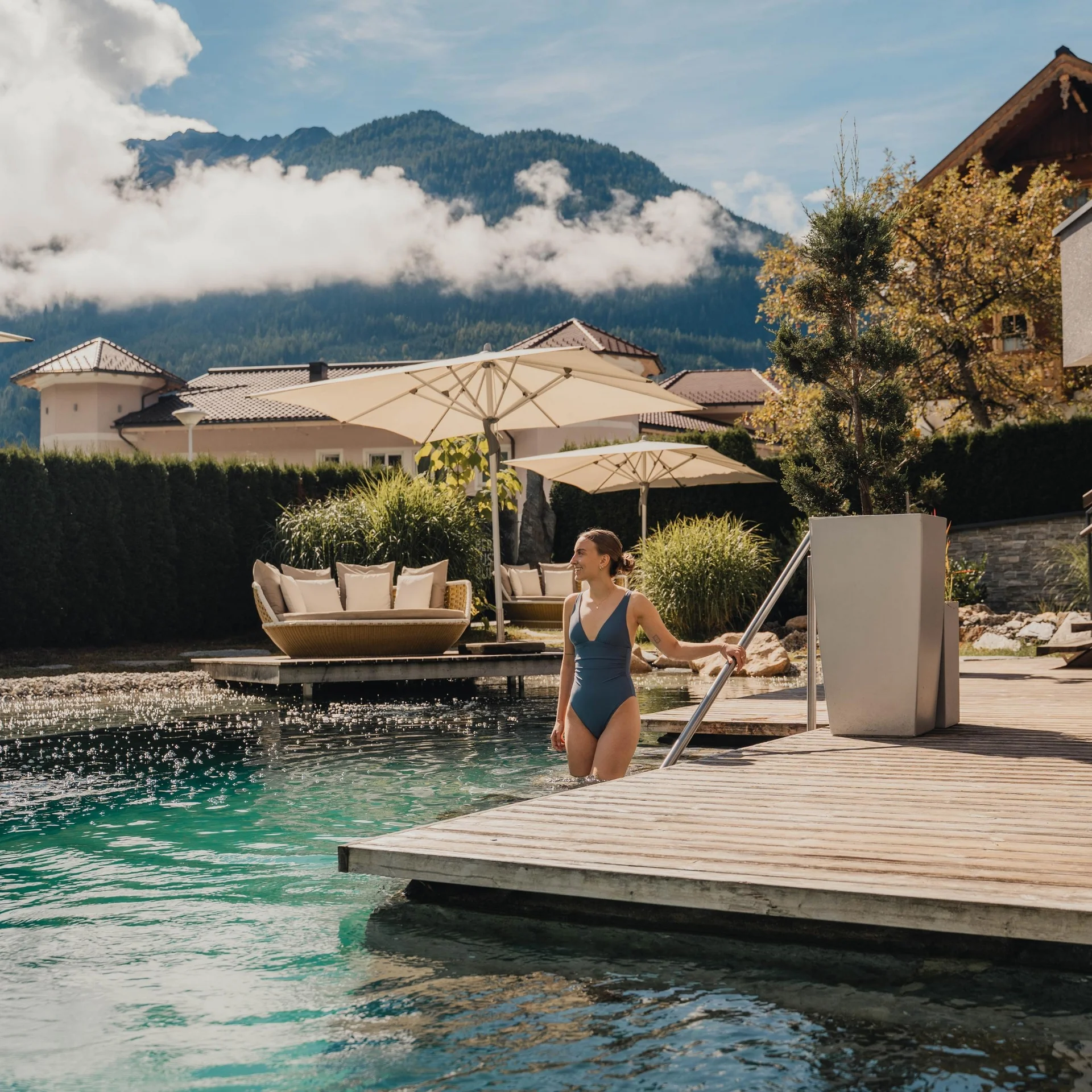 Home Frau steigt in Pool an sonnigem Tag mit Bergen und Liegen im Hintergrund