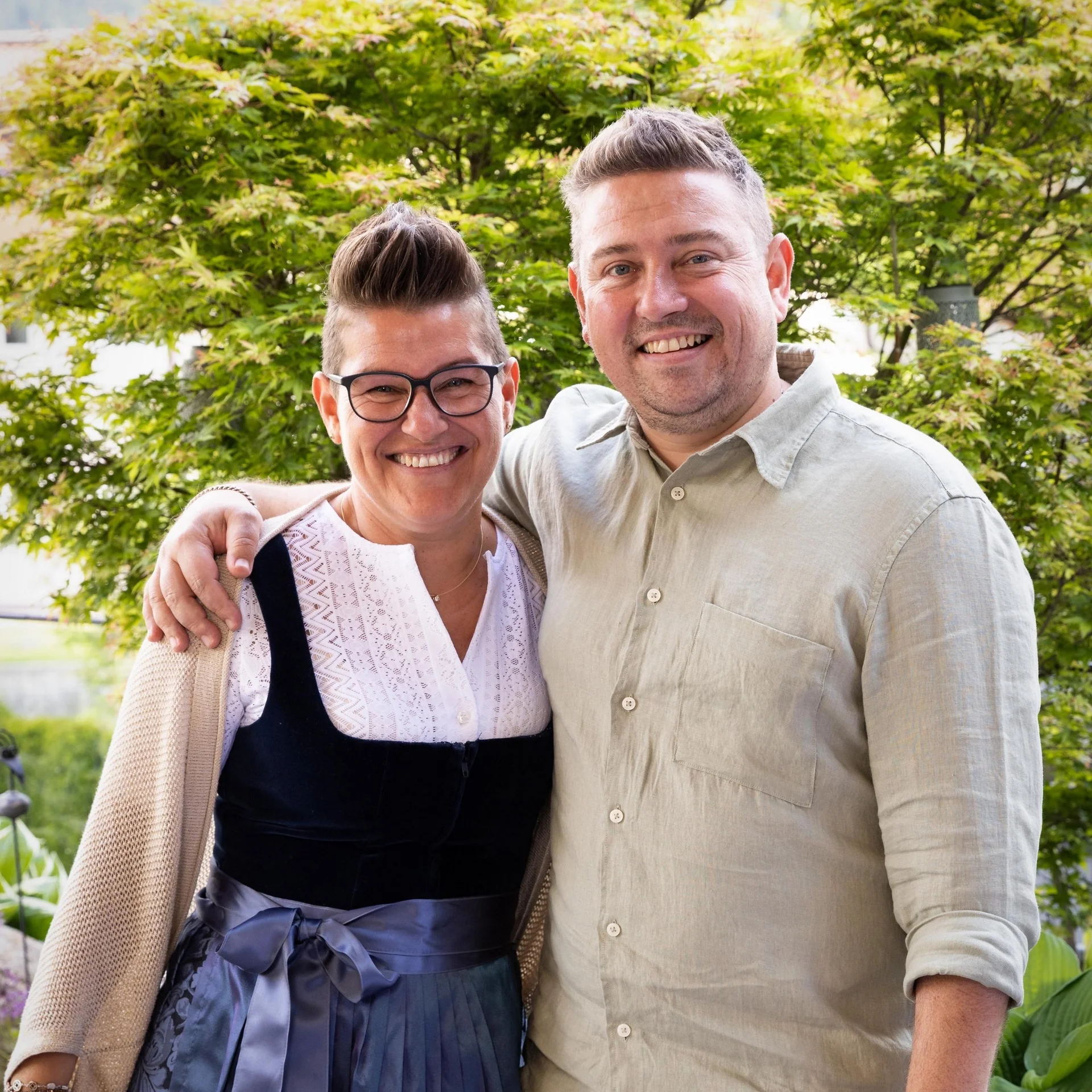 Home Zwei lächelnde Personen umarmen sich vor grünen Bäumen im Freien