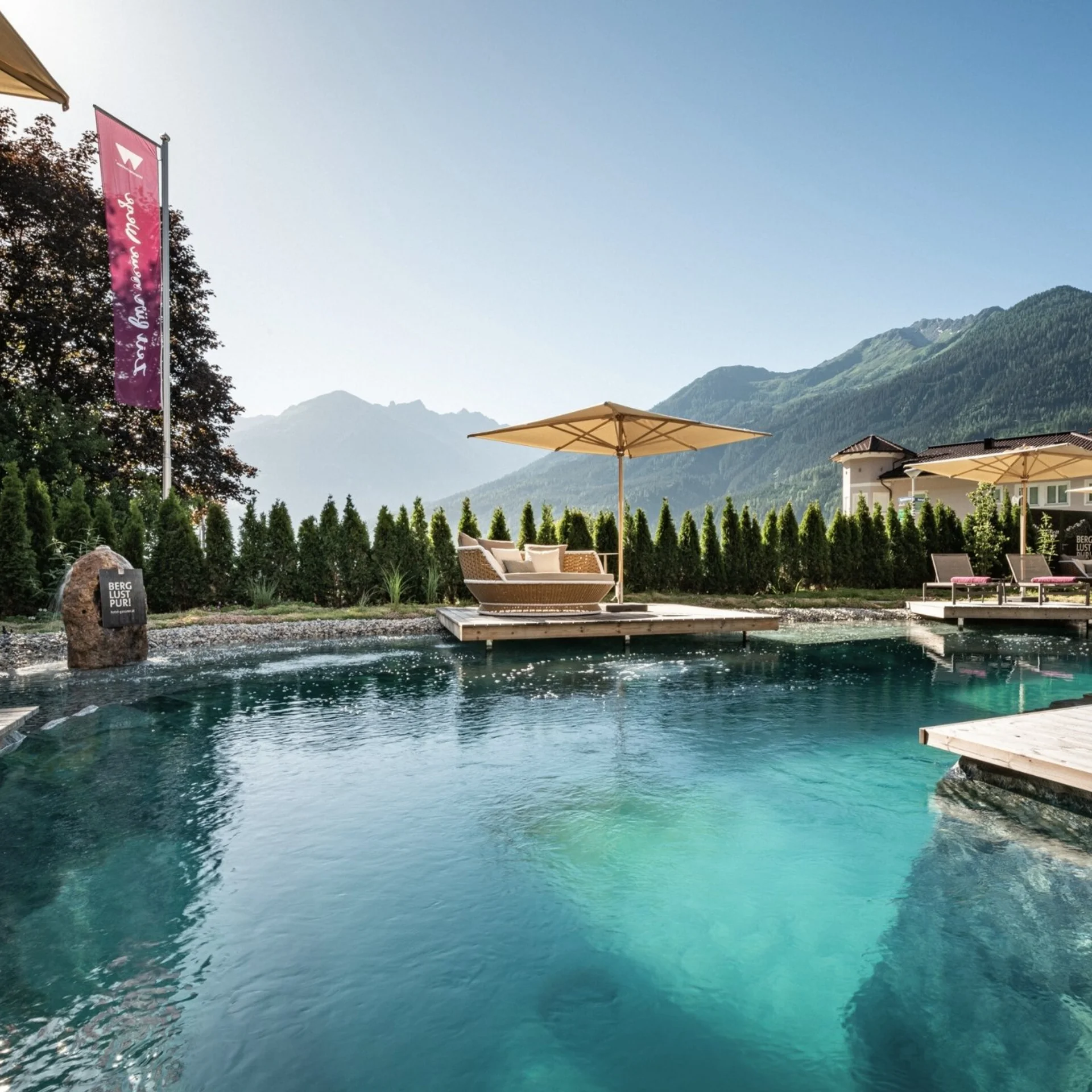 Home Außenpool mit Liegestühlen und Sonnenschirmen vor Bergkulisse