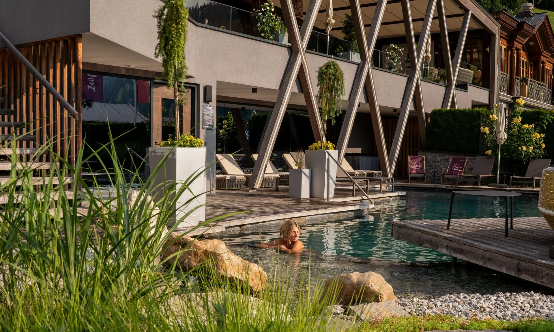 Home Frau entspannt im Außenpool eines modernen Hotels mit Holzterrasse und Pflanzen