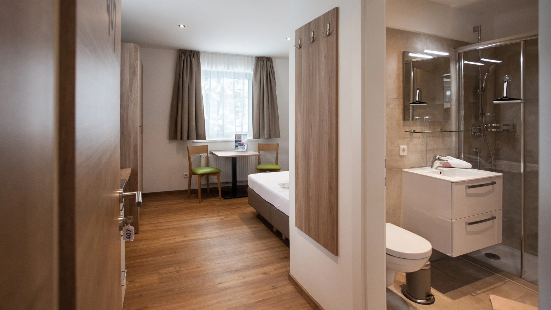Benefits im Hotel Kleines Hotelzimmer mit Holzfußboden, Bett, Tisch mit Stühlen und angrenzendem Bad