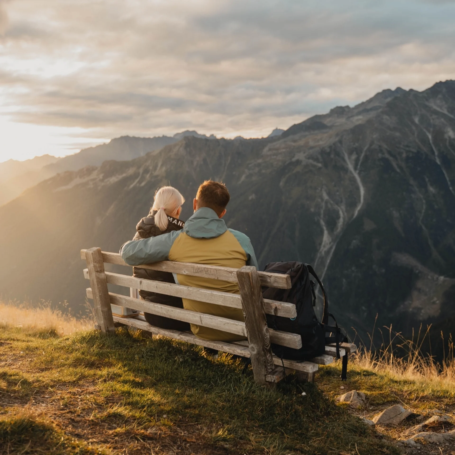 Wanderhotel Paar sitzt auf Bank und schaut bei Sonnenuntergang auf Berge