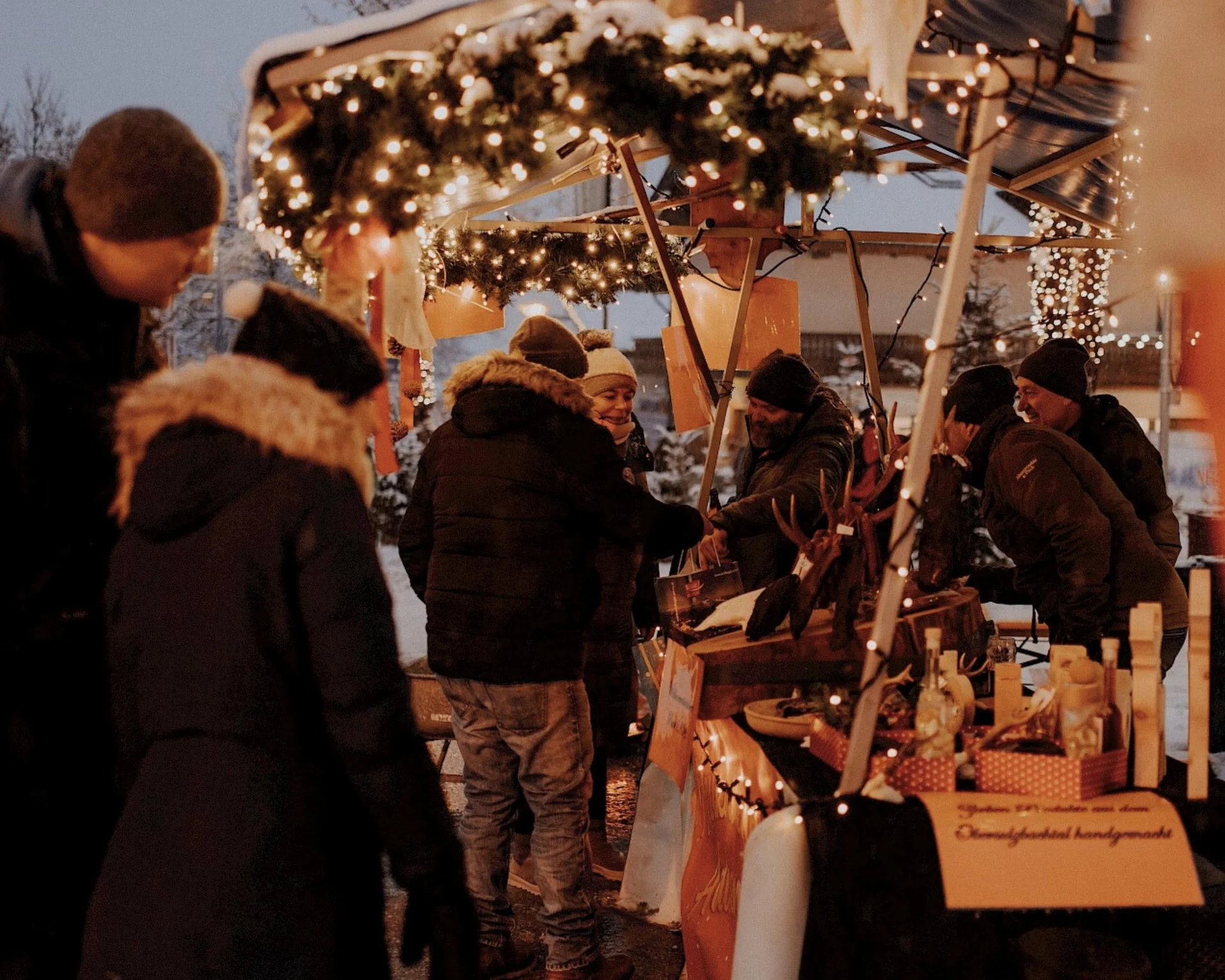 Ausflugstipps Menschen begutachten Produkte eines Weihnachtsmarktstand auf dem Adventmakt in Neukirchen am Großvenediger im Winter