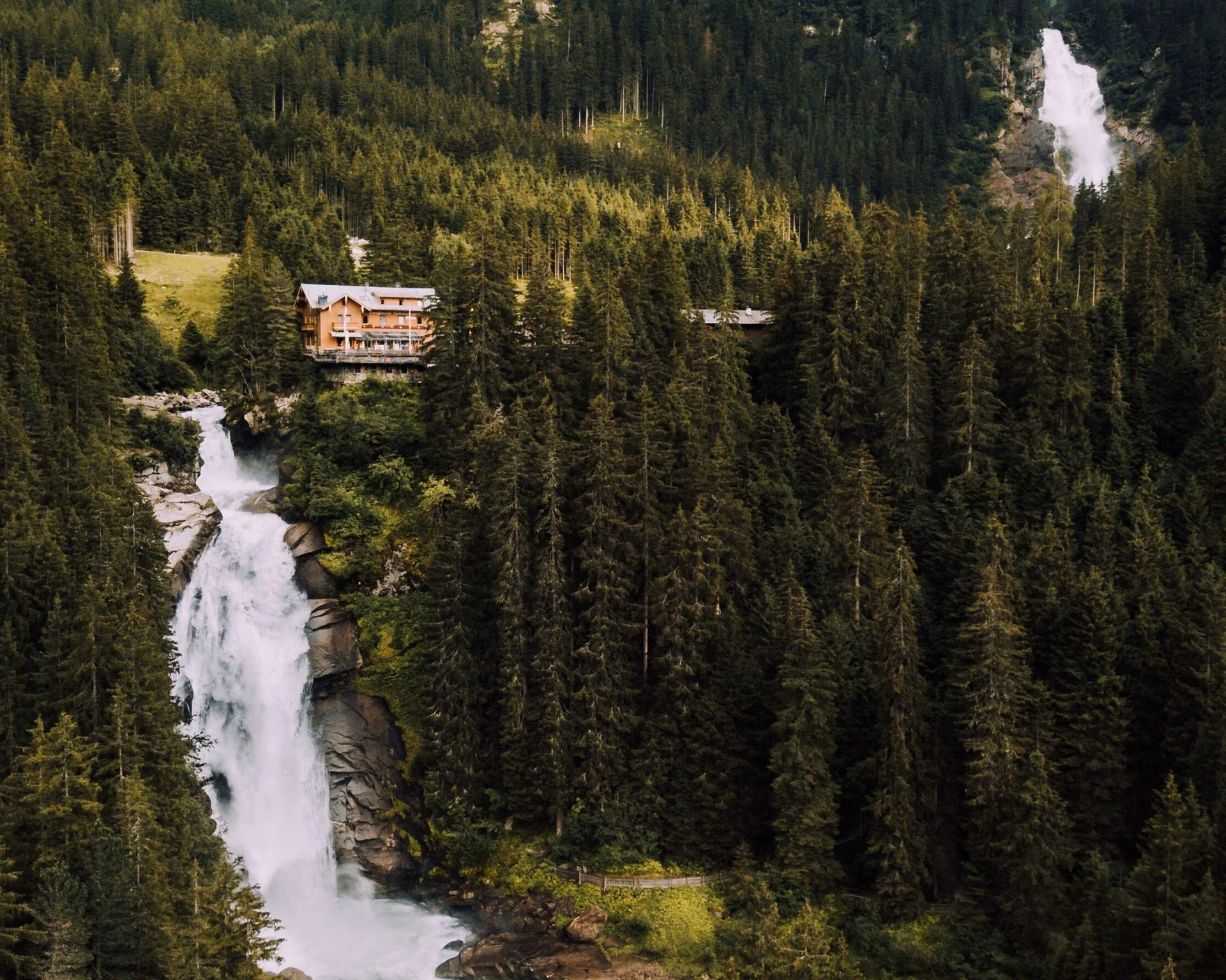 Ausflugstipps Blick auf einen der oberen Wasserfälle der Krimmler Wasserfälle in bewaldeter Berglandschaft und einem Gasthaus