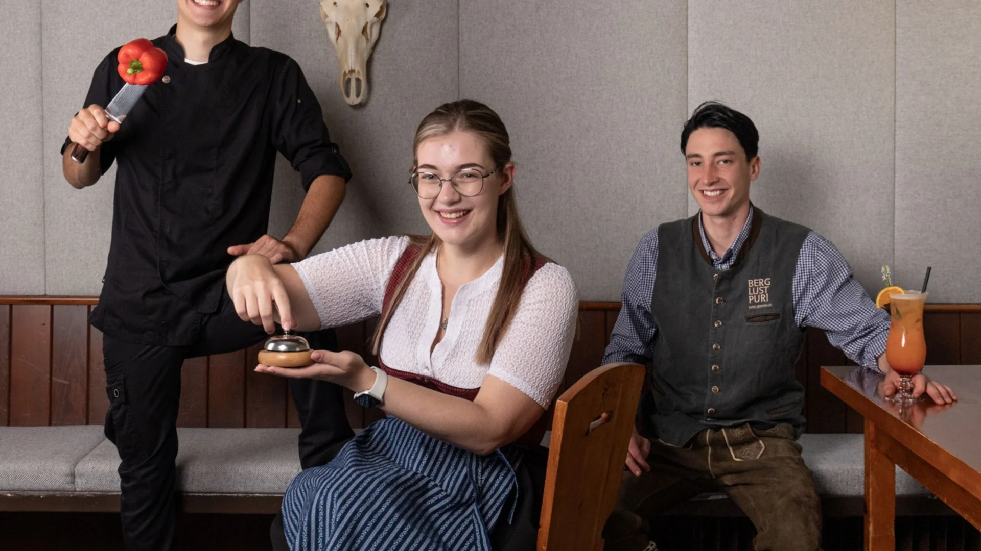 Lehrlingsausbildung Drei junge Menschen in traditioneller und moderner Kleidung in einer Gasthausstube