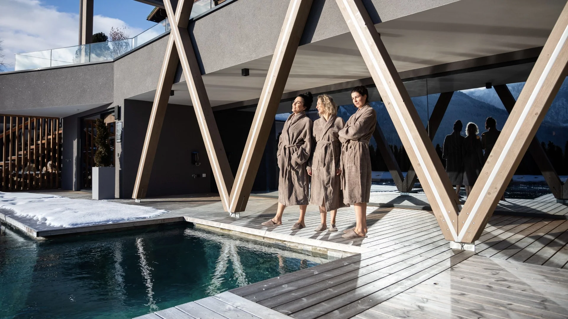 Saunawelt Drei Frauen in Bademänteln stehen auf Holzsteg neben Pool im modernen Gebäude