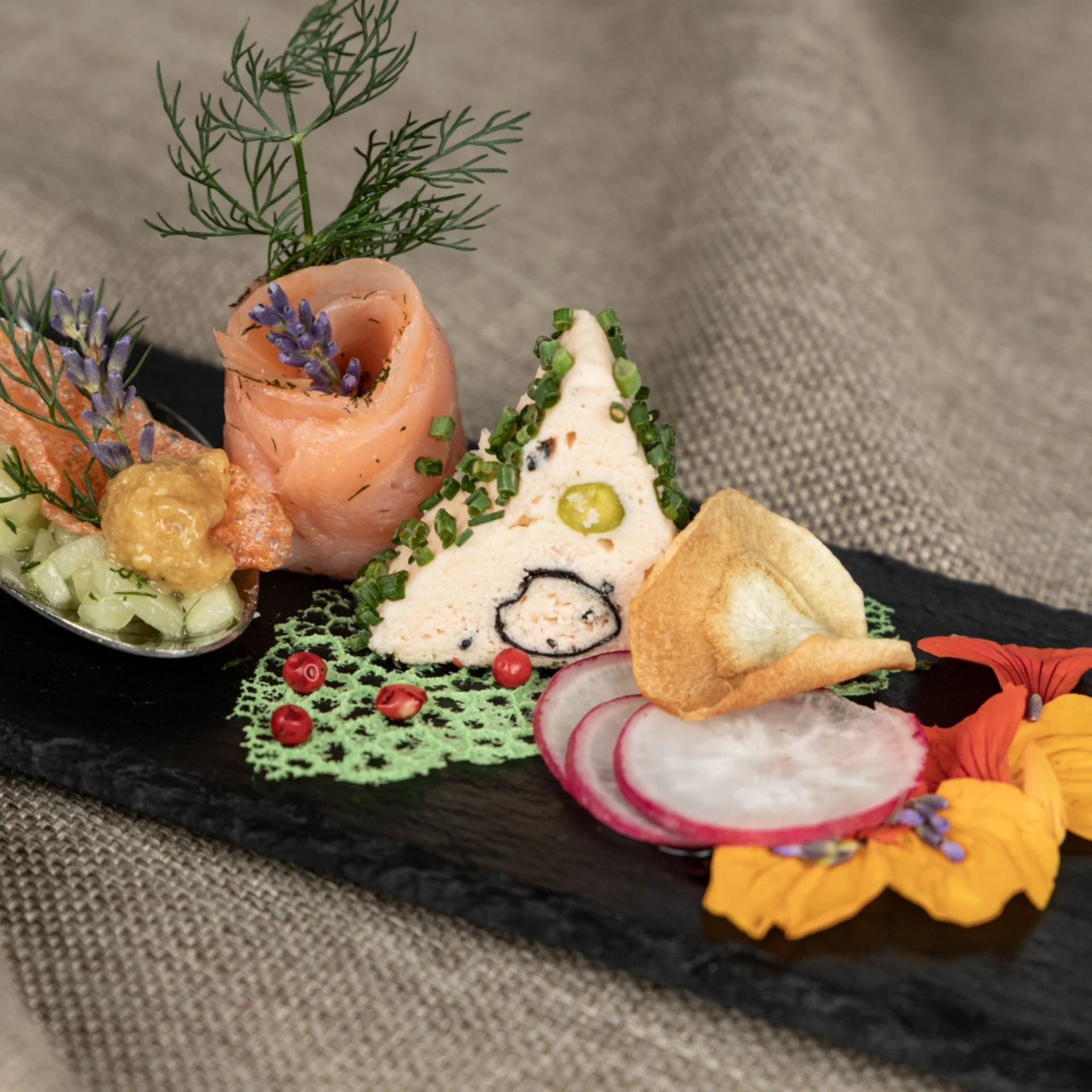 Kulinarik Kunstvoll angerichtete Vorspeise mit Lachs, Kräutern und Gemüse auf Schieferplatte