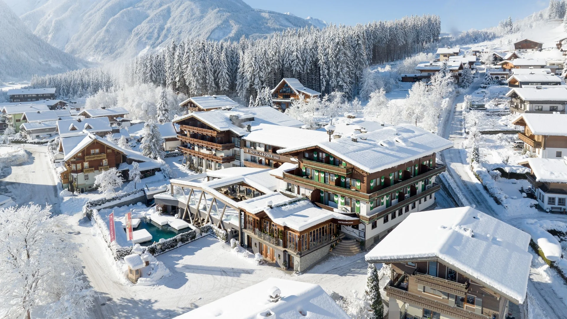 Lage + Anreise Verschneites Hotel und Häuser in einem alpinen Winterdorf mit Bergen im Hintergrund