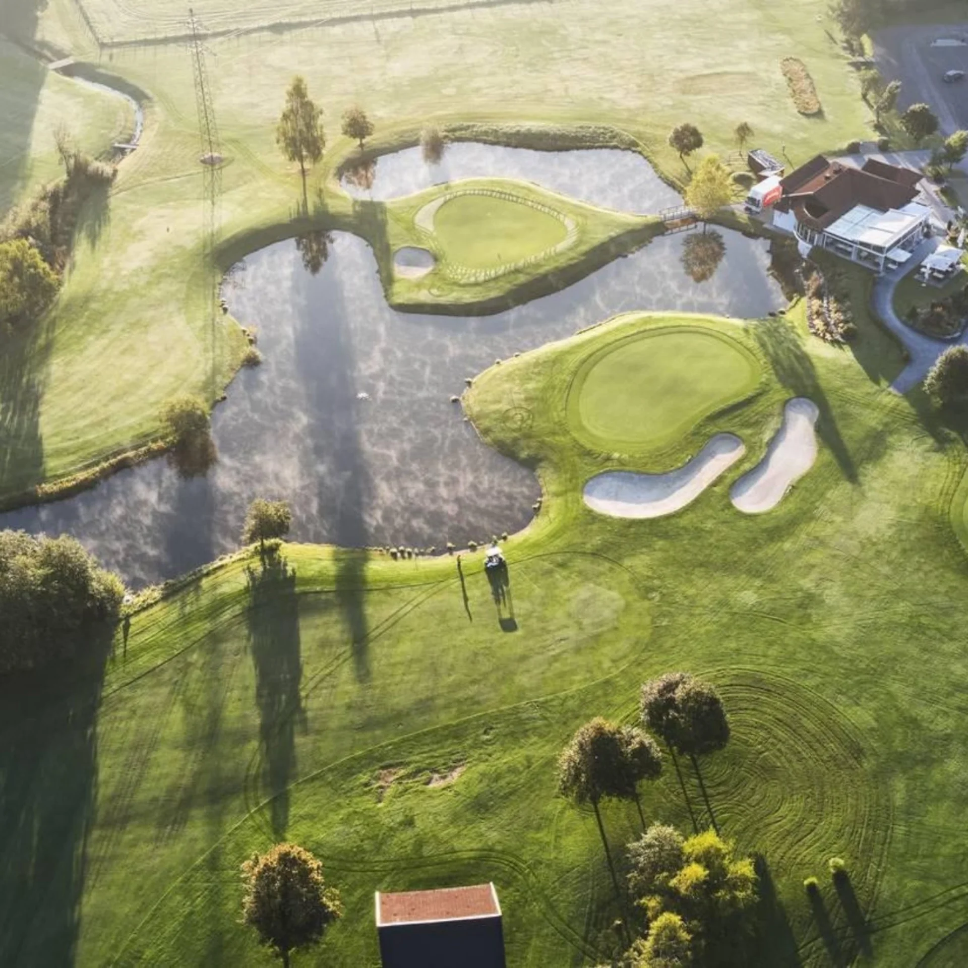 Bergsommer Luftaufnahme eines Golfplatzes mit Teichen und Clubgebäuden bei Sonnenlicht