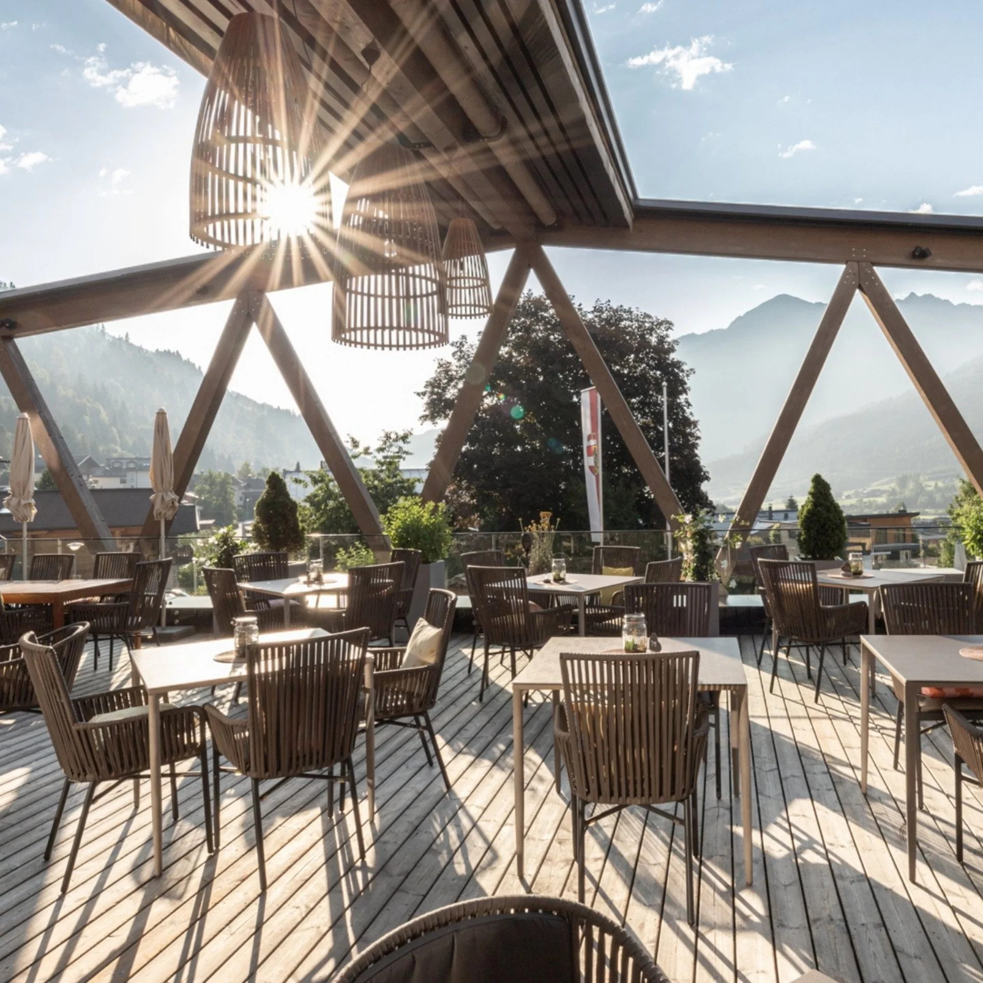 Kulinarik Sonnige Terrasse mit Tischen und Stühlen und Berglandschaft im Hintergrund