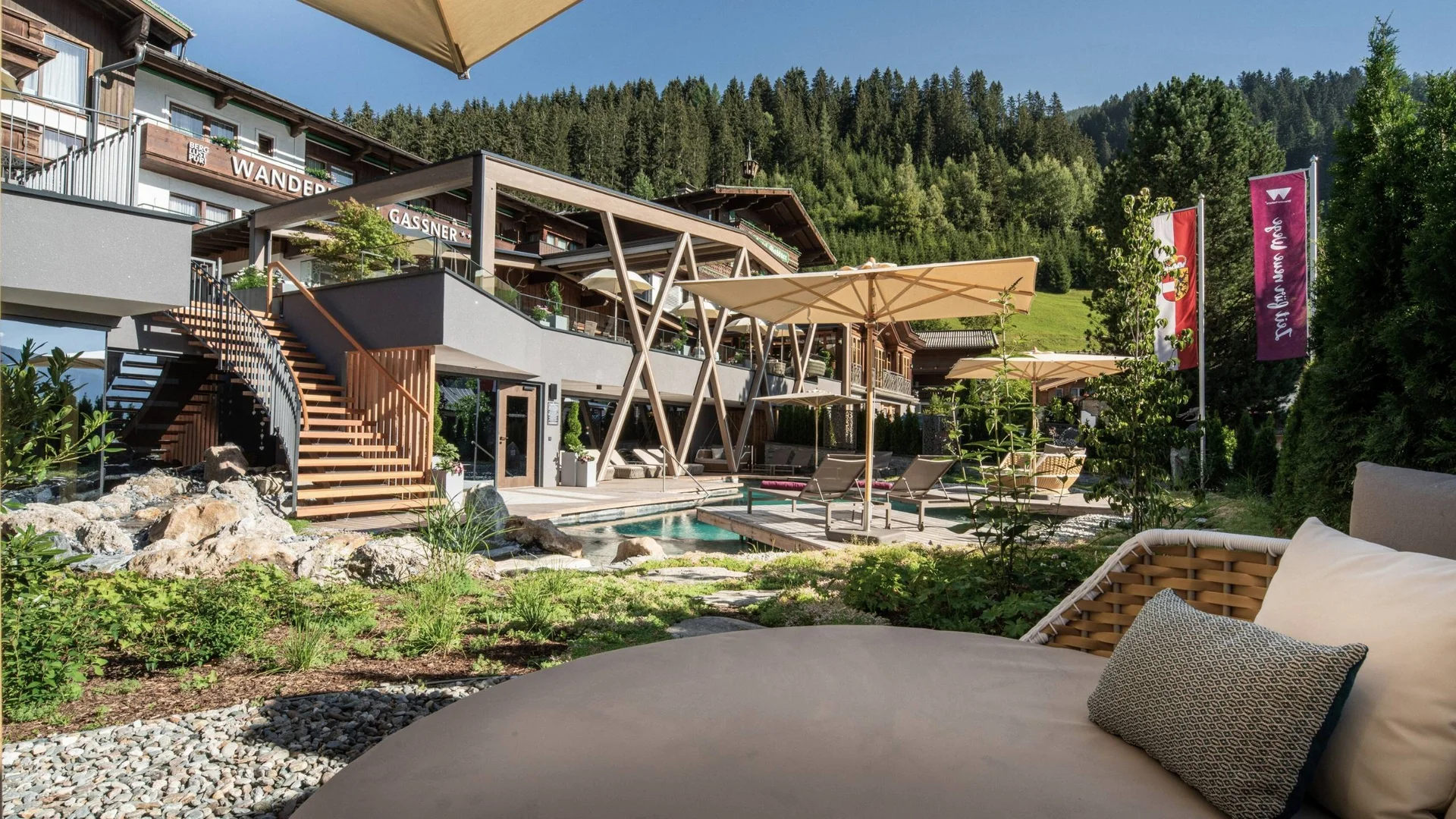 Wellness Außenbereich eines Hotels mit Pool, Sonnenschirmen und Bergen im Hintergrund