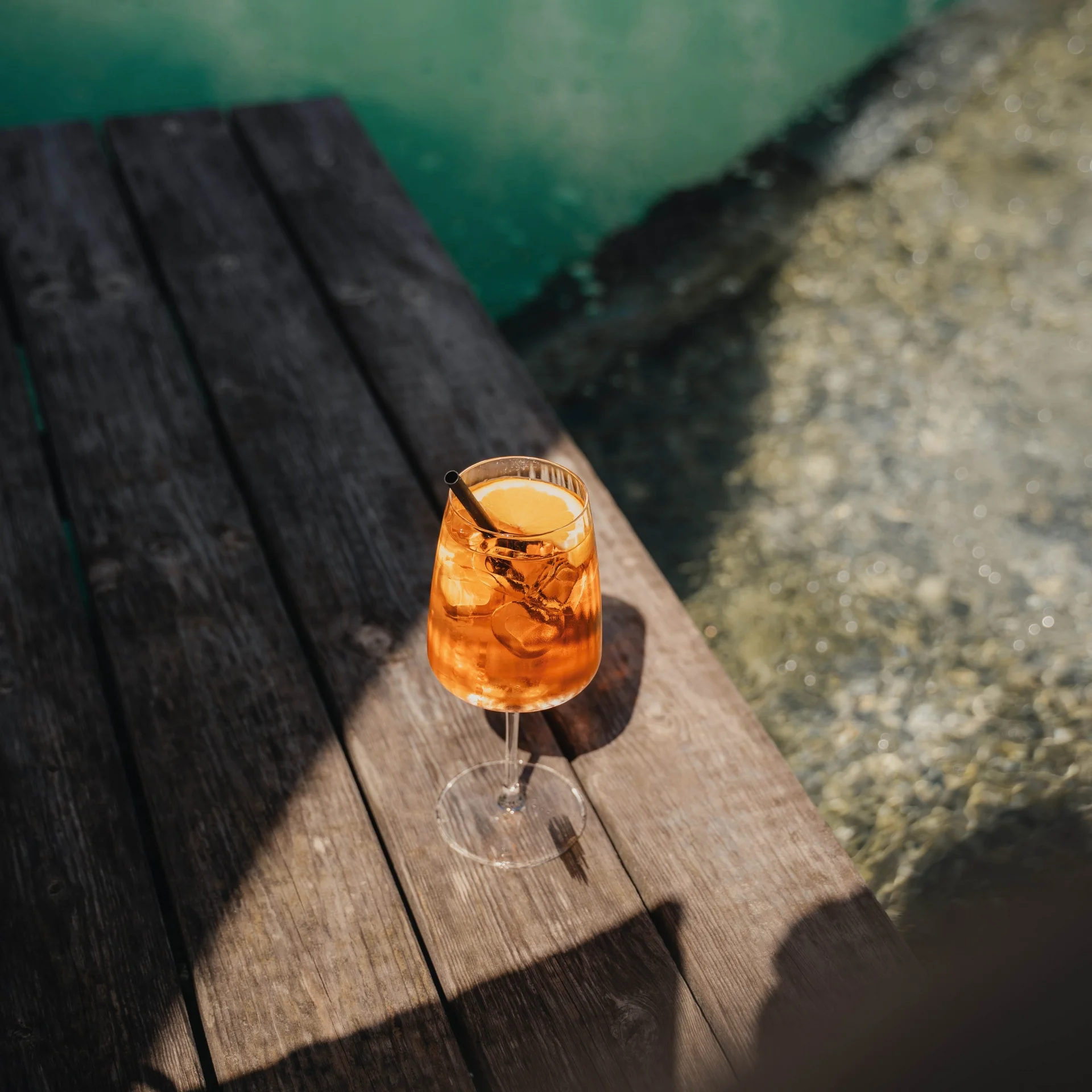 Wellness Ein Glas Aperol Spritz mit Eis und Orangenscheibe auf Holzterrasse am Wasser