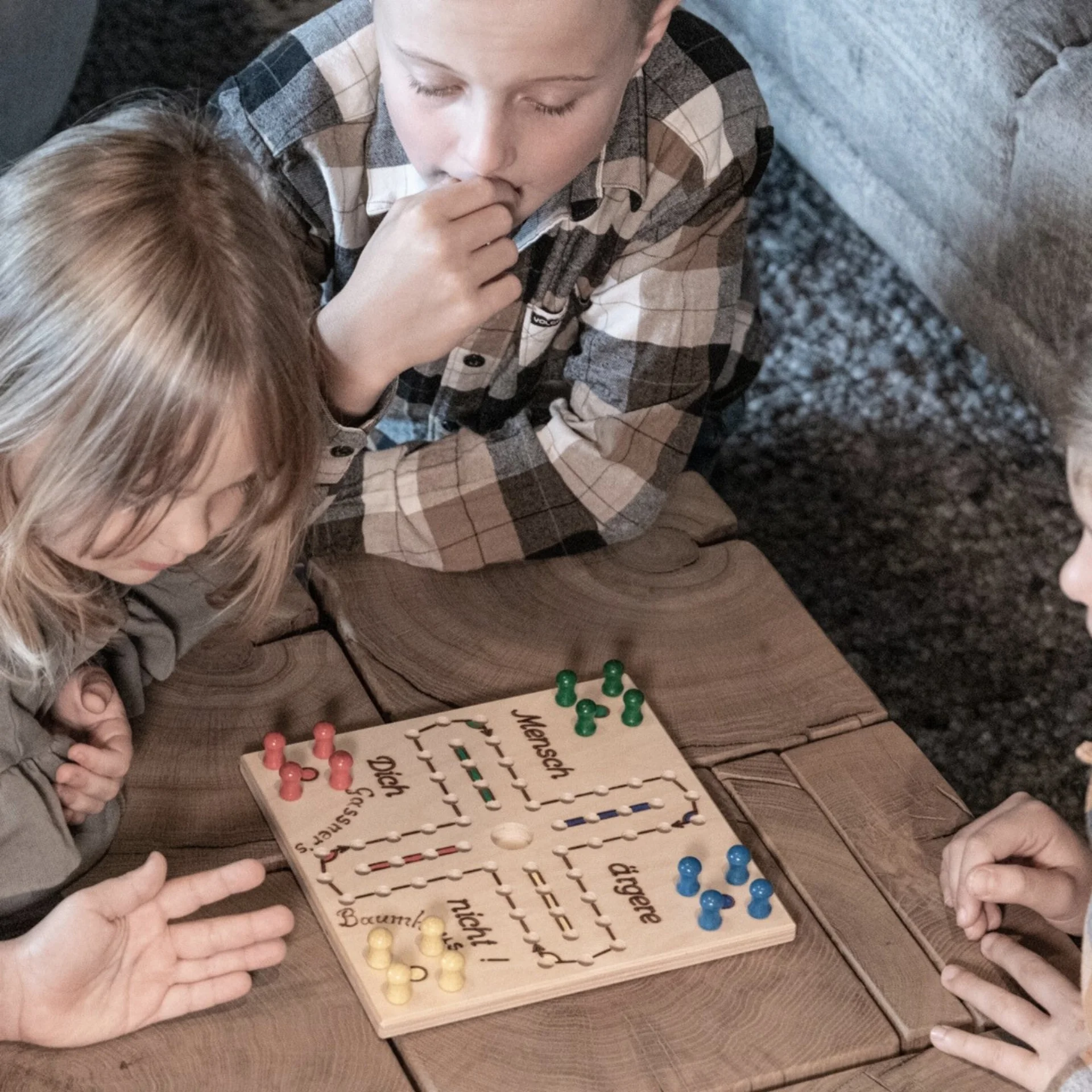Familienzeit Vier Kinder spielen Mensch-ärgere-dich-nicht auf einem Holztisch
