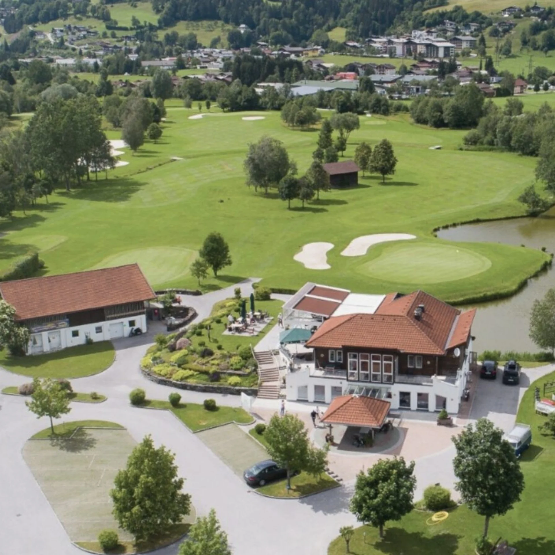 Golfen Luftaufnahme eines Golfplatzes mit Gebäuden, Teich und umliegendem Grünland