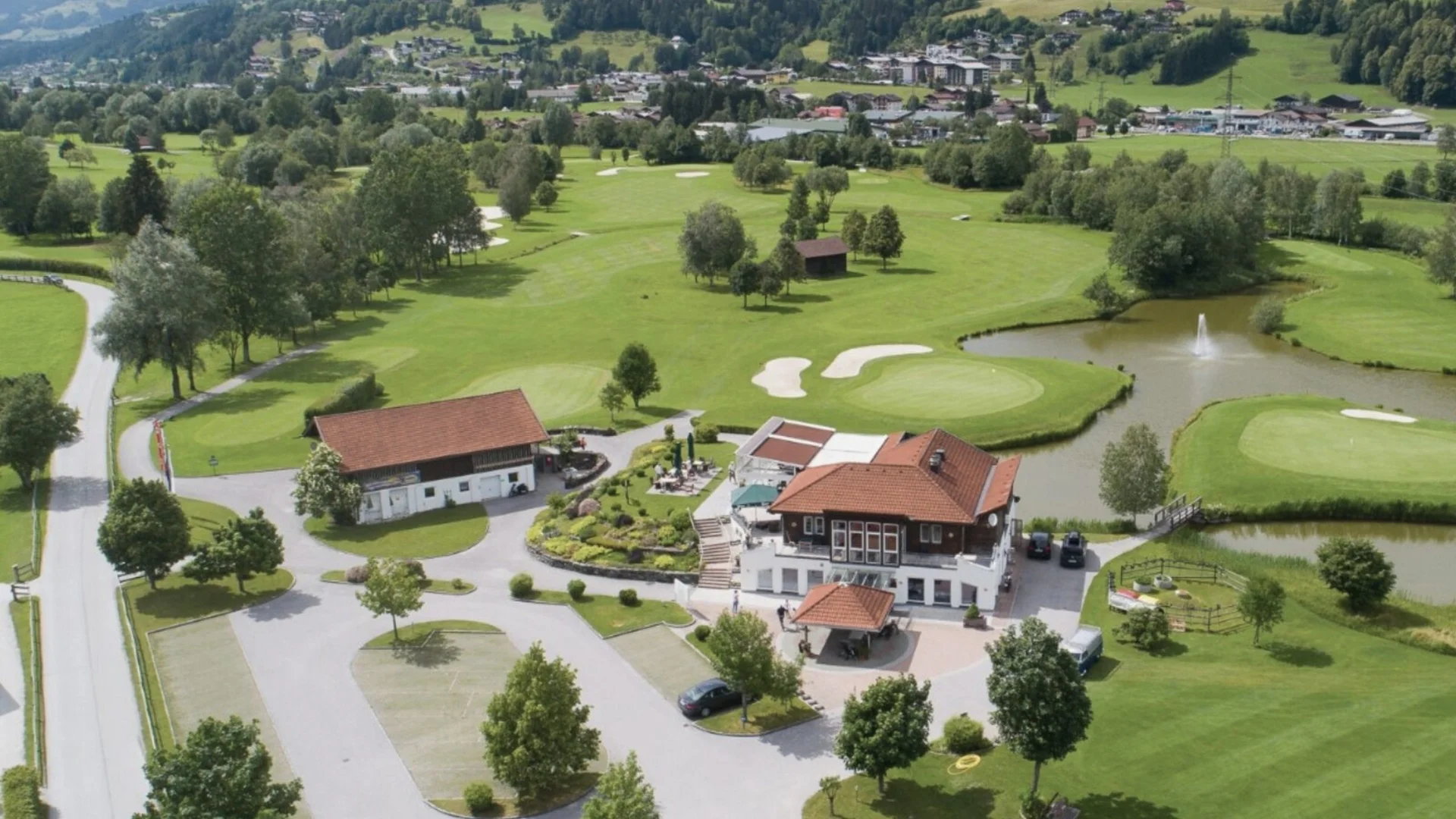 Golfen Luftaufnahme eines Golfplatzes mit Gebäuden, Teich und umliegendem Grünland
