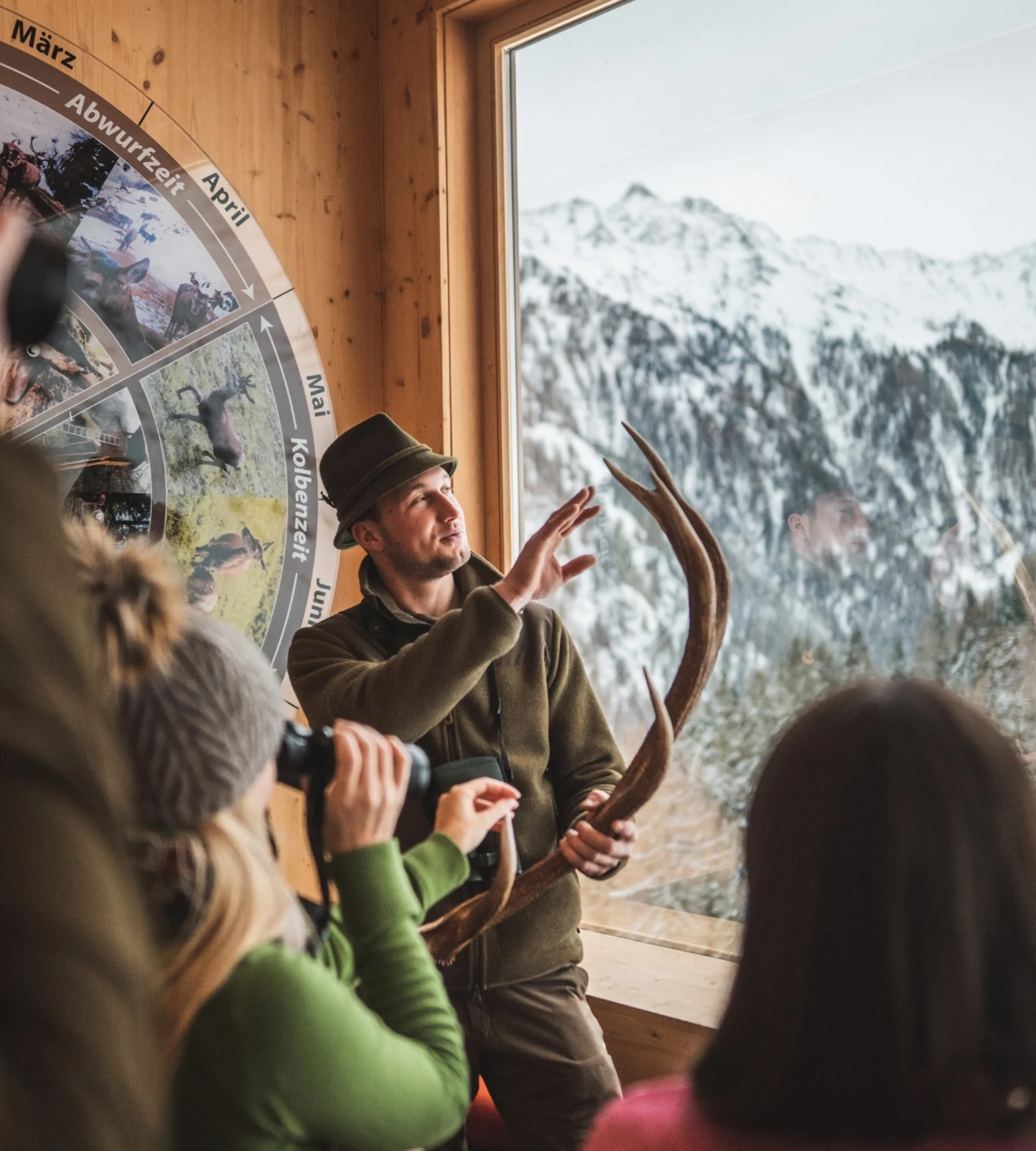 Bergwinter Jäger erklärt Hirschgeweih vor verschneiter Berglandschaft mehreren Personen