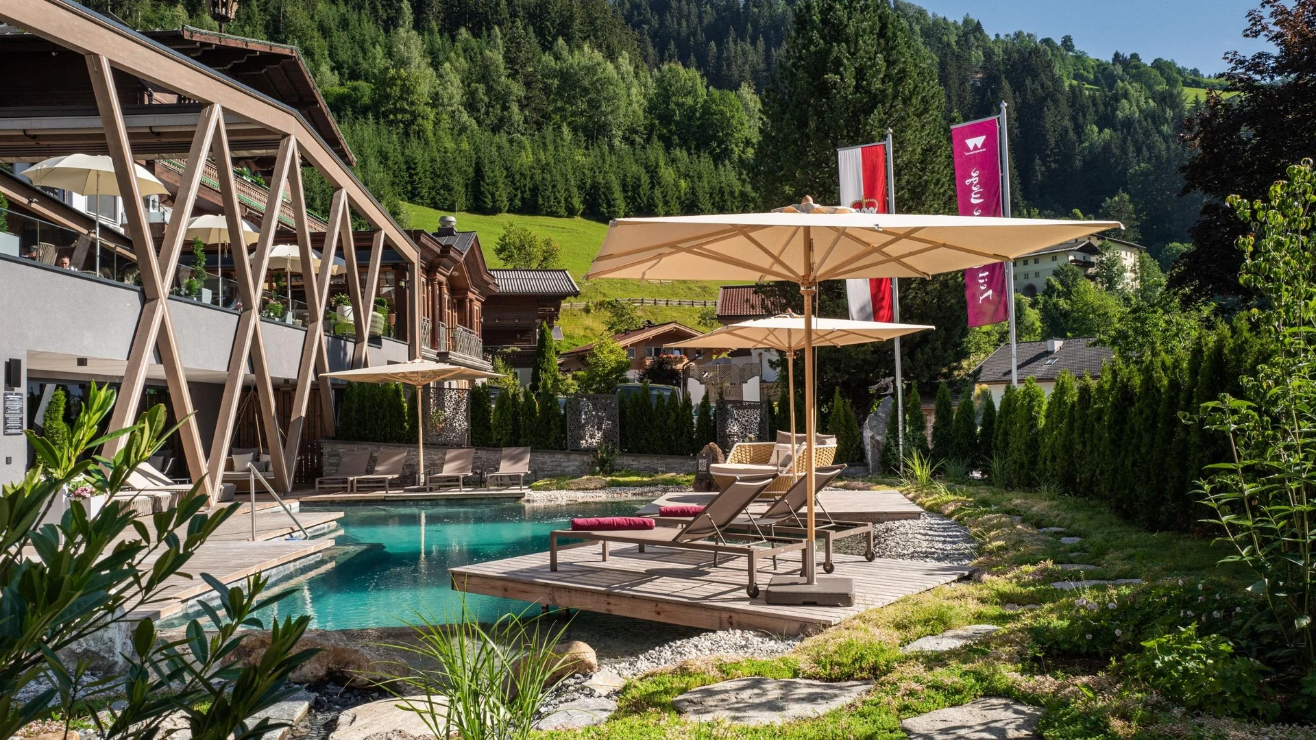 Saunawelt Entspannungsbereich mit Pool, Liegestühlen und Sonnenschirmen vor bewaldetem Hügel