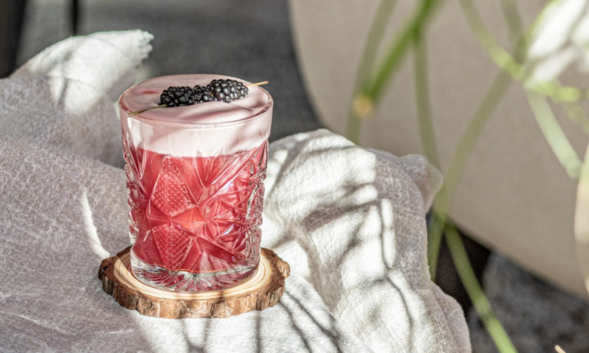 Home Rotes Getränk mit Schaum und Brombeeren in einem verzierten Glas auf Holzuntersetzer