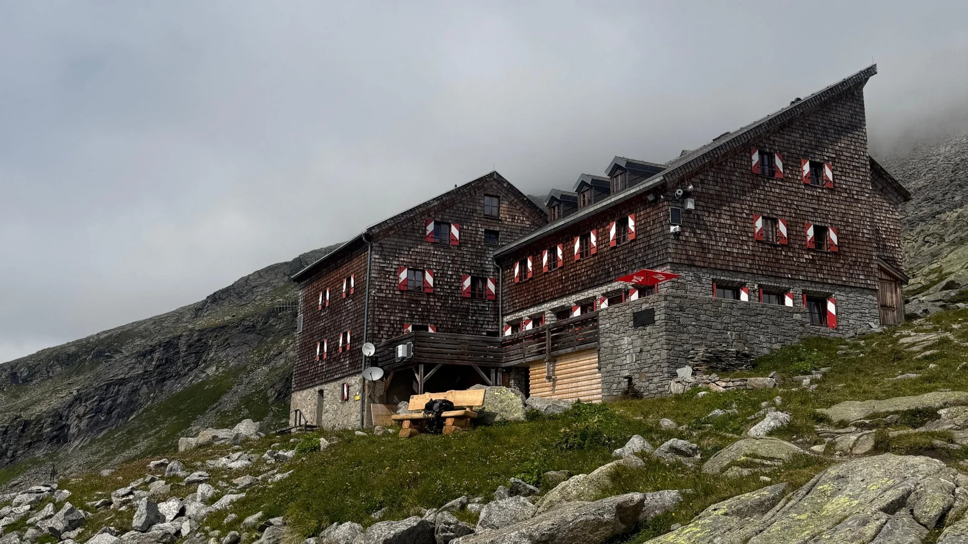 Großvenediger Almhütte auf einem grasigen, felsigen Berghang bei bewölktem Himmel