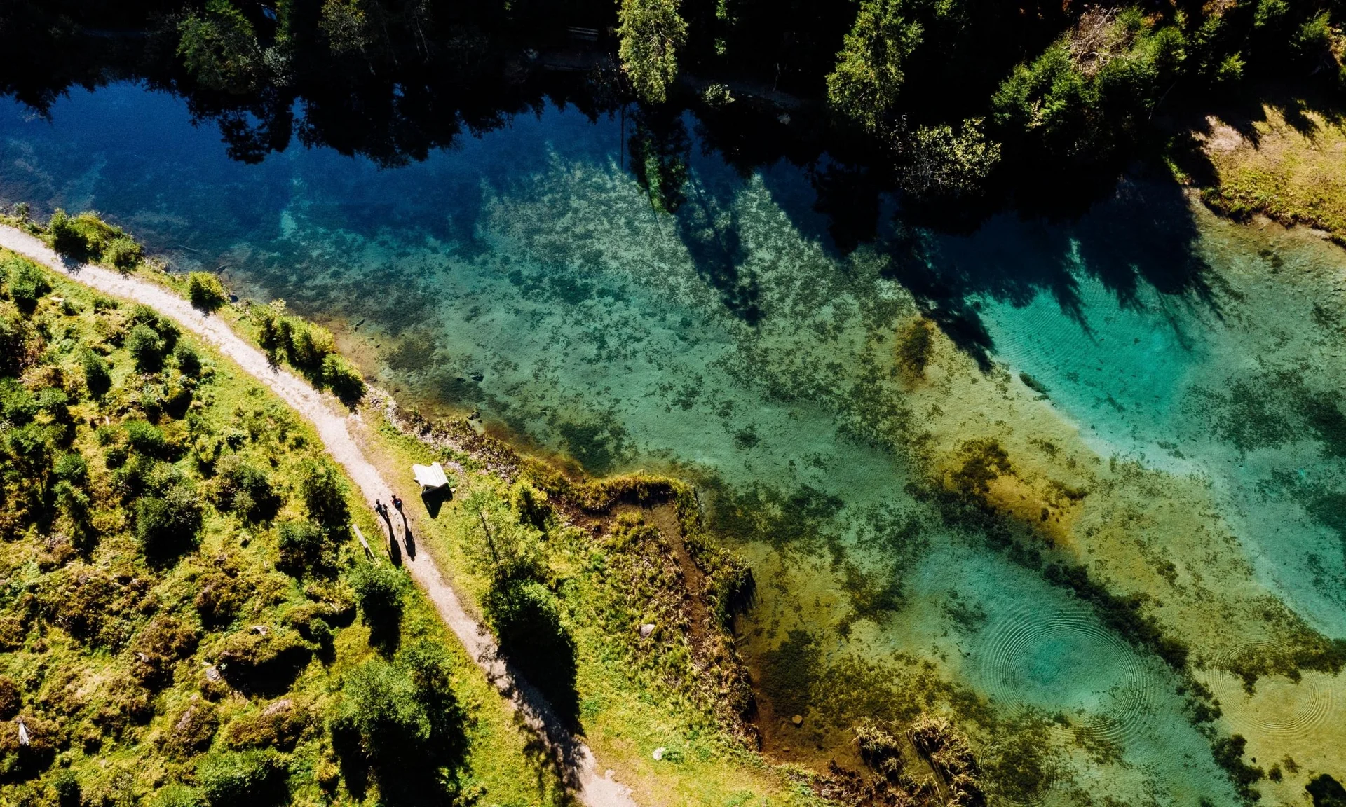 Wanderhotel Luftaufnahme von einem Pfad neben klarem Fluss und Wald im Sonnenschein