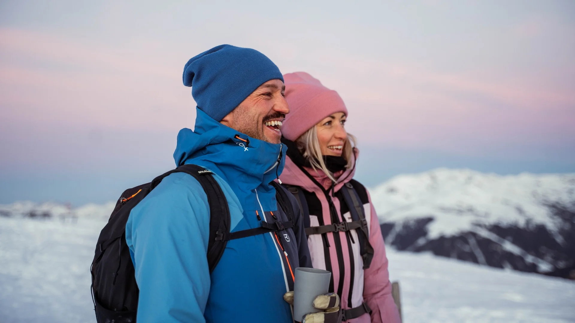Wanderservice Fröhliches Paar in Winterkleidung bei Sonnenuntergang in verschneiter Berglandschaft
