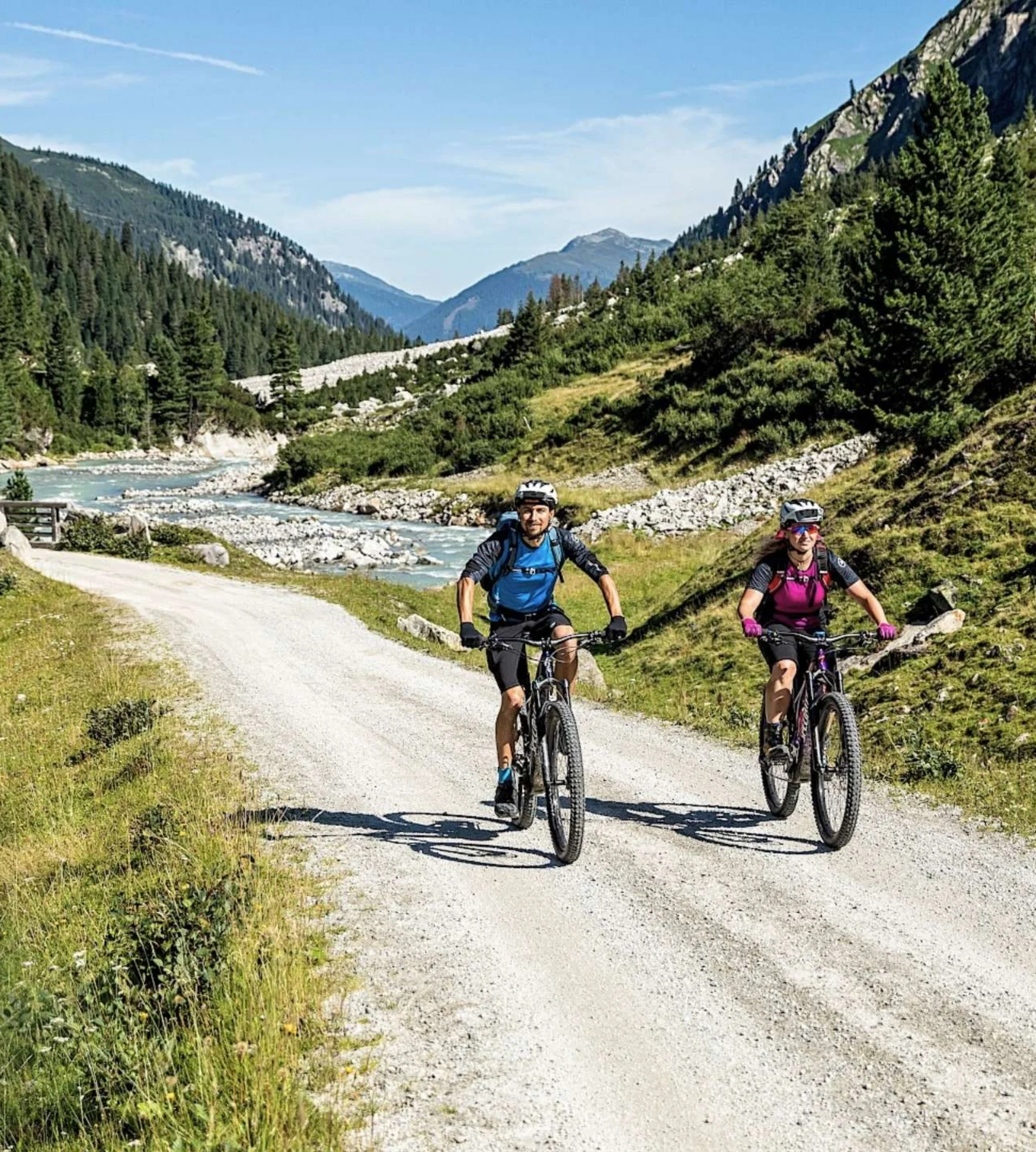 Nationalpark Sommercard Zwei Radfahrer fahren auf einem Bergweg neben einem Fluss bei sonnigem Wetter