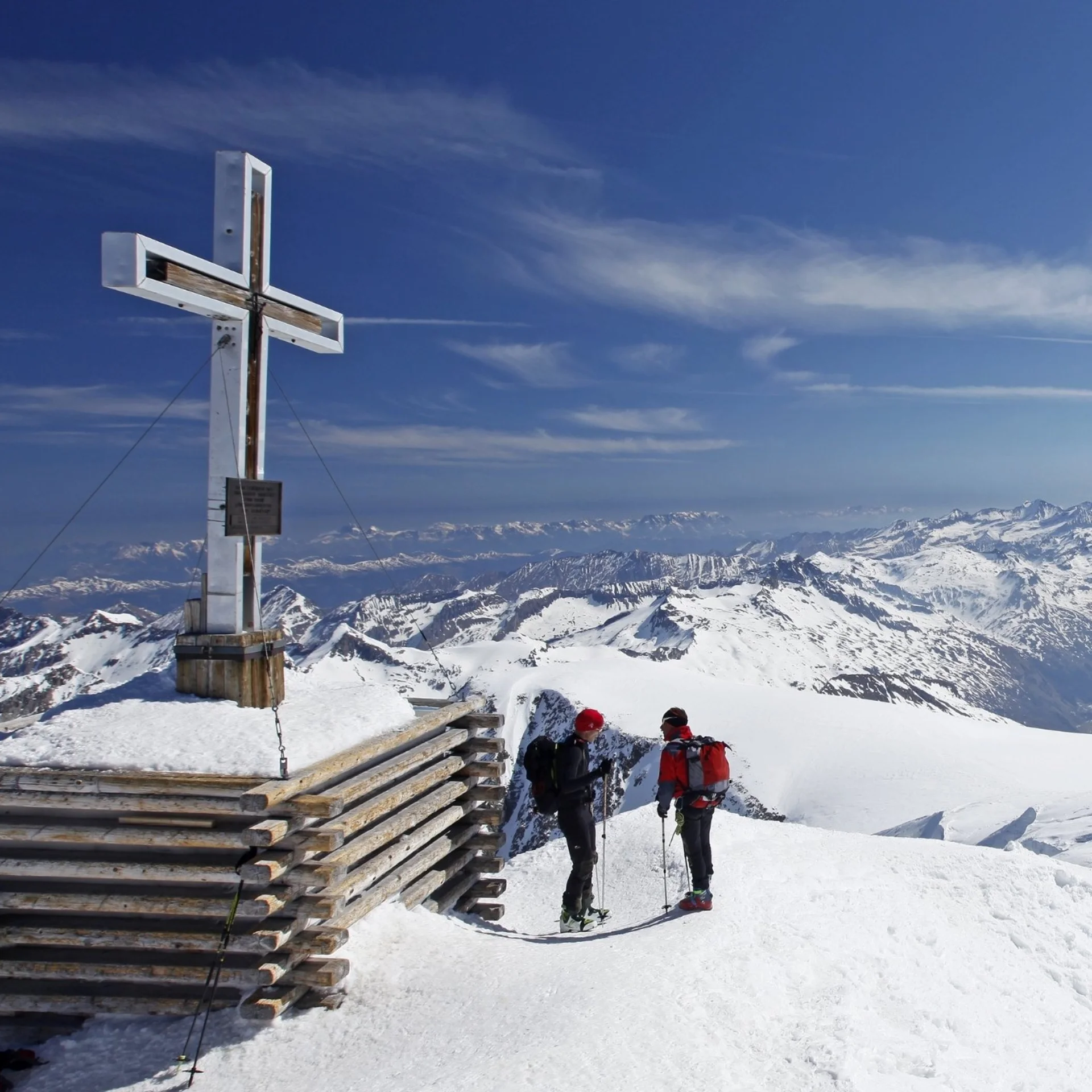 Abseits der Piste Gipfelkreuz auf schneebedecktem Berg mit Wanderern und Bergpanorama