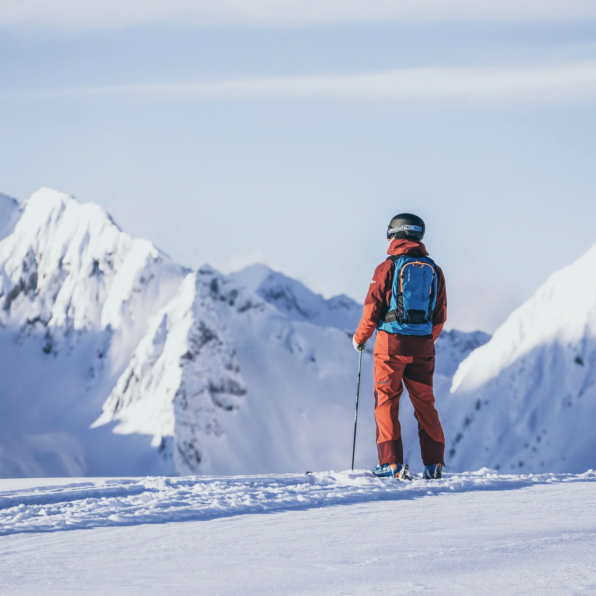 Skifahren Skifahrer in roter Kleidung mit Rucksack vor verschneiten Bergen