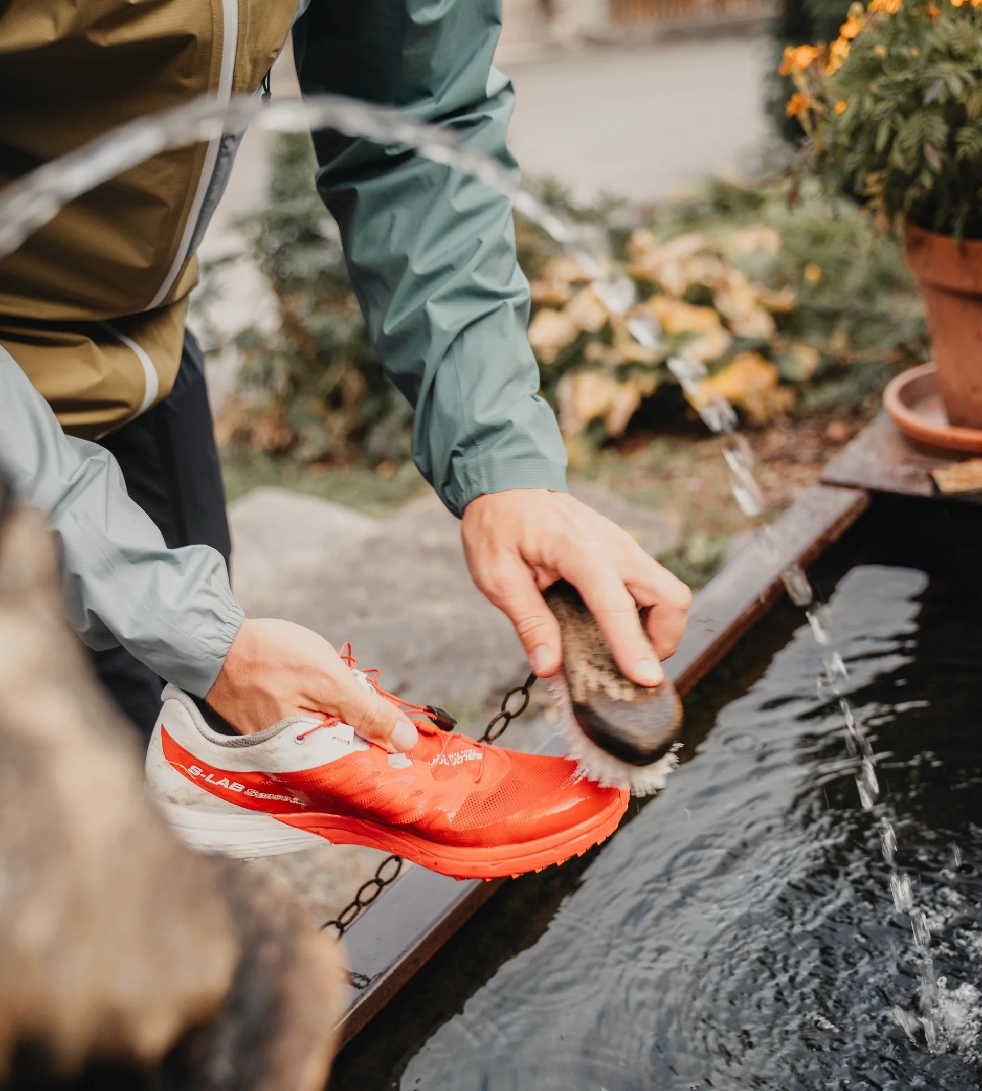Wanderhotel Person reinigt roten Sportschuh mit Bürste an Wasserquelle