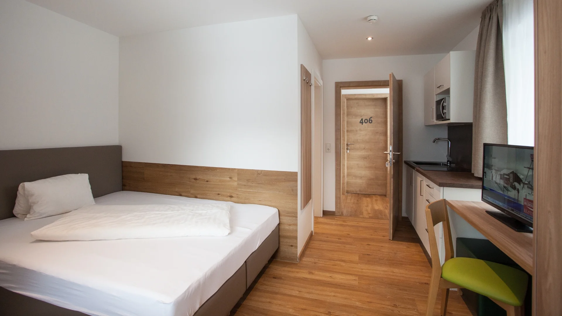 Benefits im Hotel Kleines Hotelzimmer mit Einzelbett, Schreibtisch, TV und offener Tür zur Flur