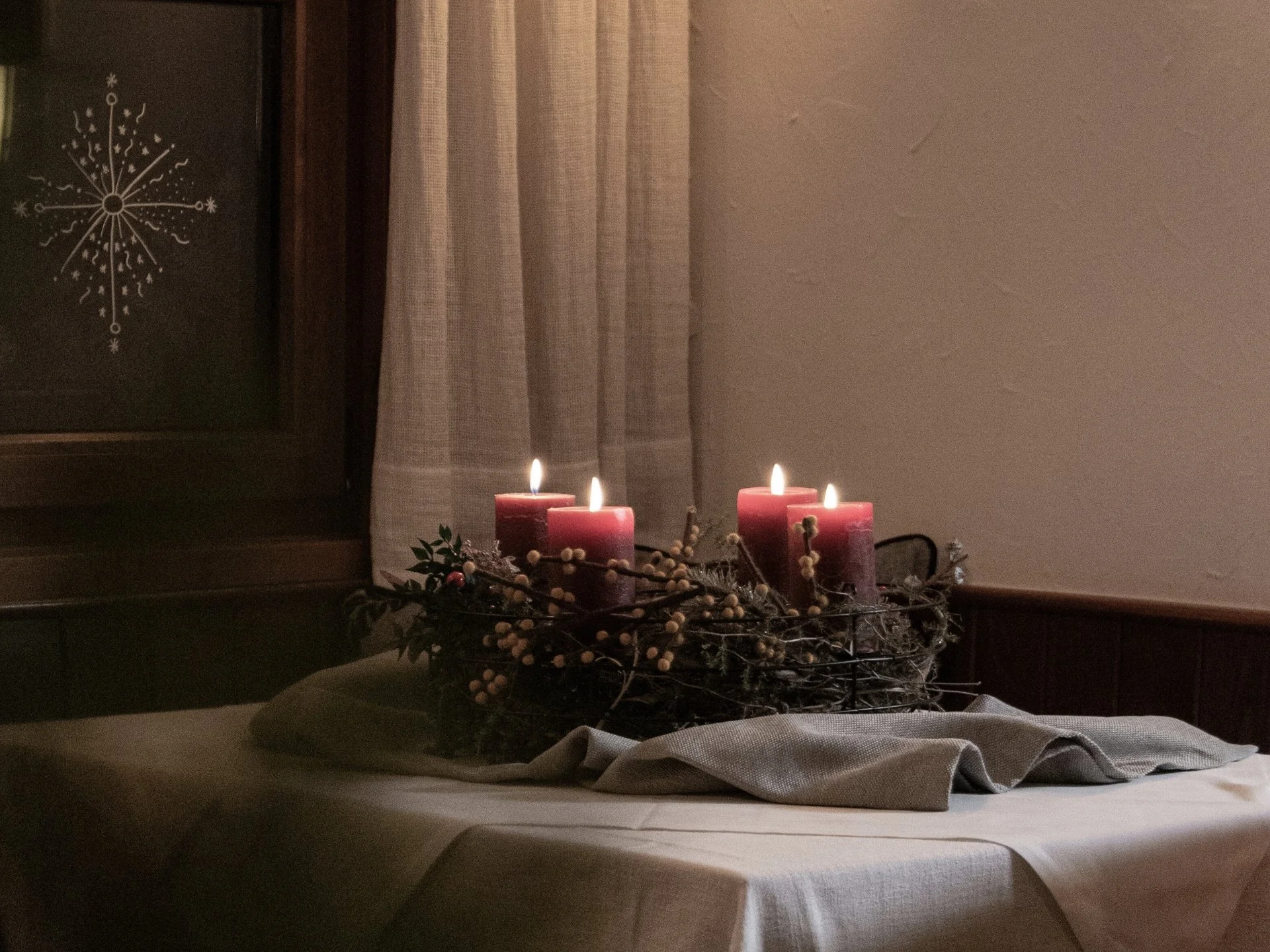 Home Vier brennende rote Kerzen auf einem mit Tuch bedeckten Tisch am Fenster