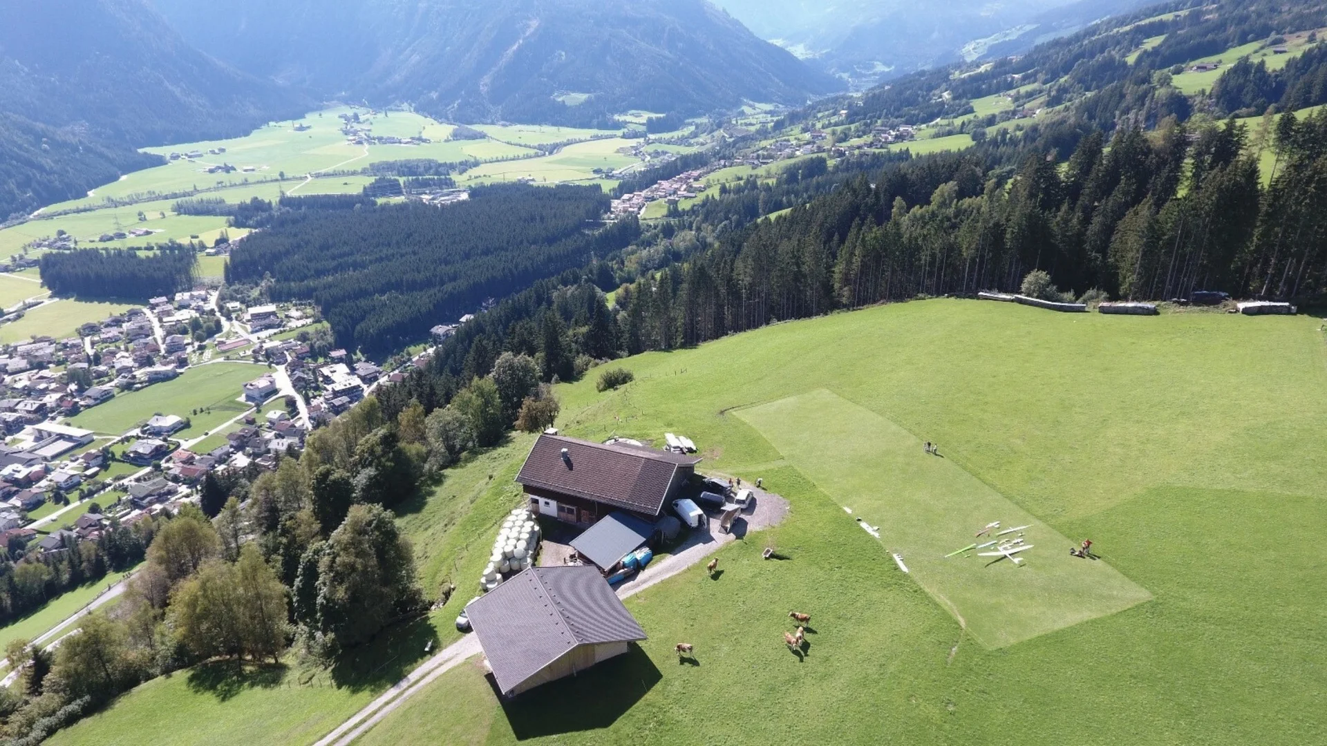 Modell- und Hangfliegen Bauernhof auf Hügel mit Graspiste und Kühen in einem grünen Tal