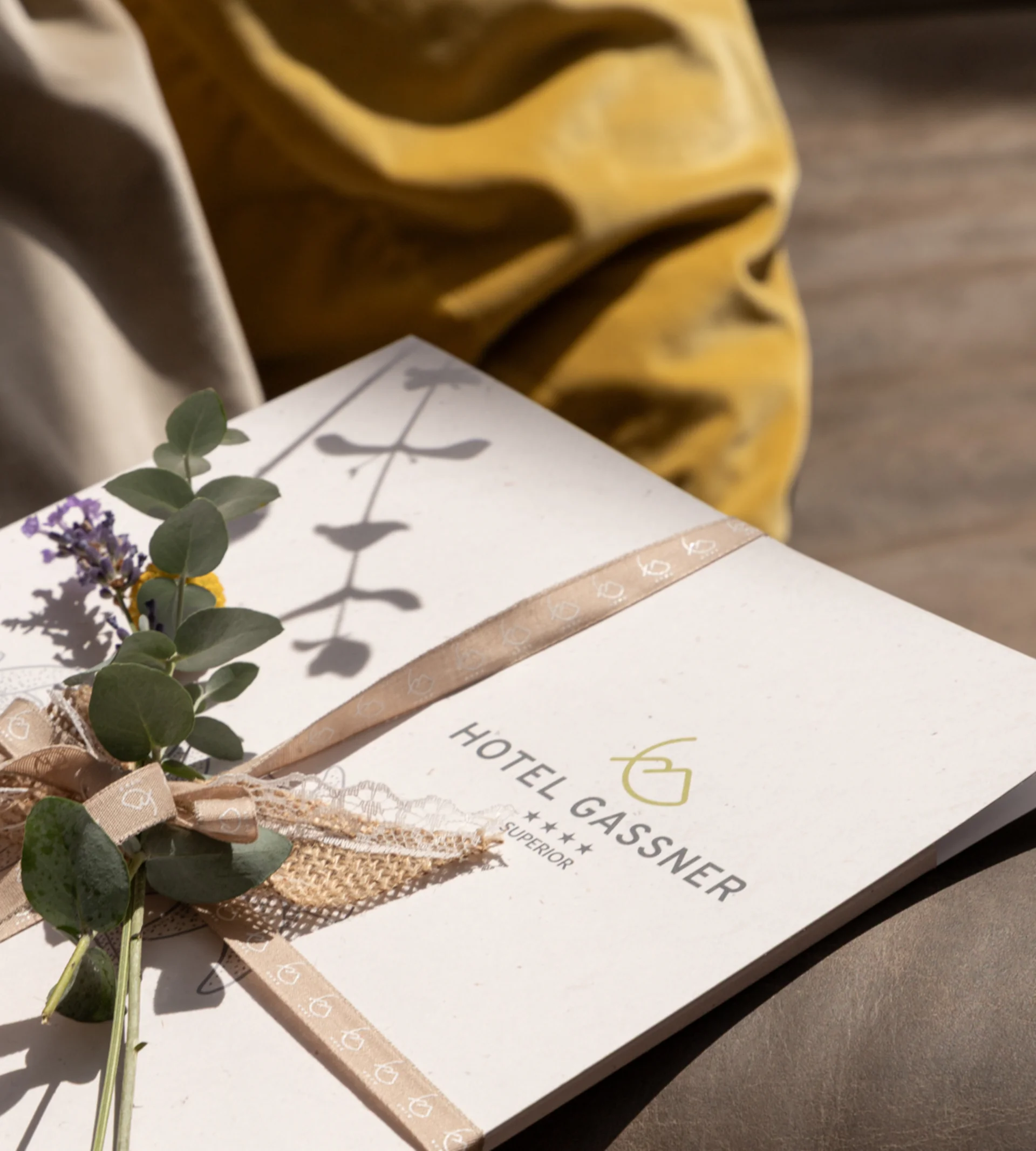 Kulinarik Geschenkverpackte Hotel Gassner Broschüre mit floralem Dekor auf einem Sofa