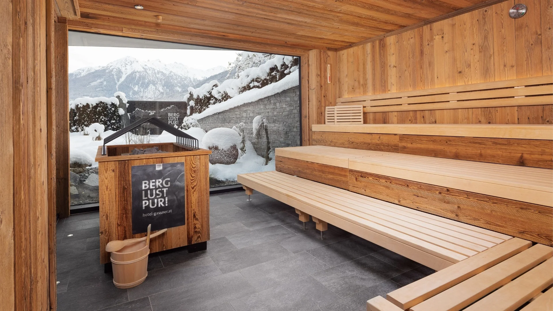 Saunawelt Sauna mit Holzinterieur und Blick auf schneebedeckte Berge durch ein großes Fenster