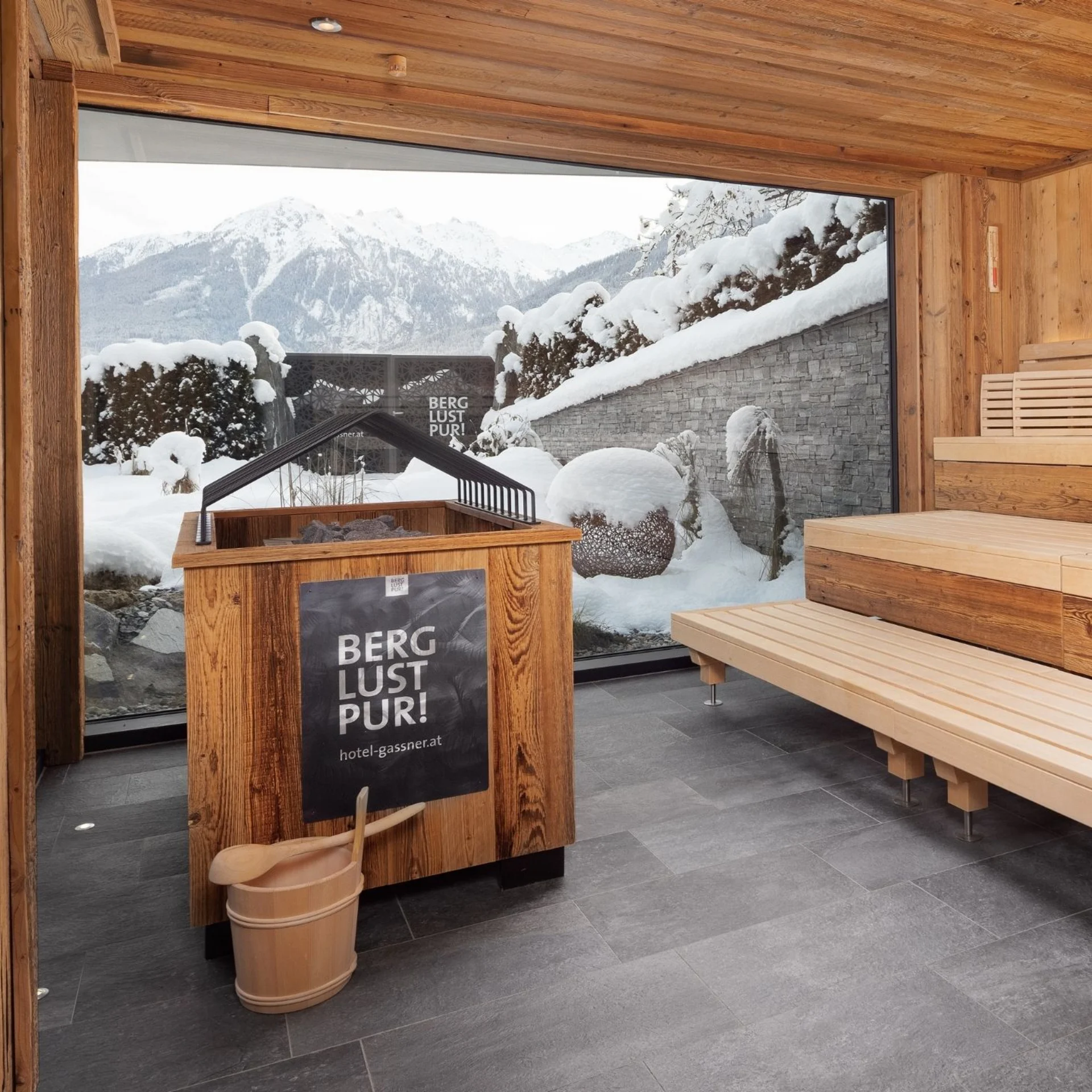 Wellness Sauna mit Holzinterieur und Blick auf schneebedeckte Berge durch ein großes Fenster