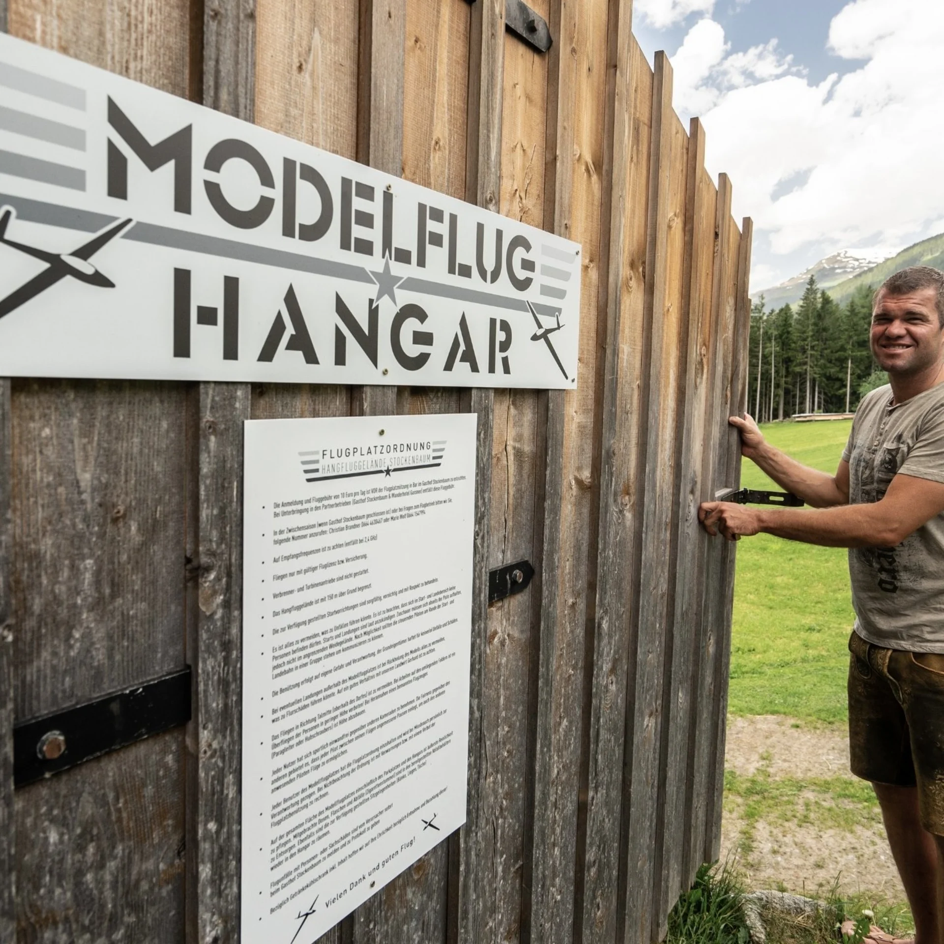 Modell- und Hangfliegen Mann öffnet Holztor zum Modellflughangar in grüner Berglandschaft