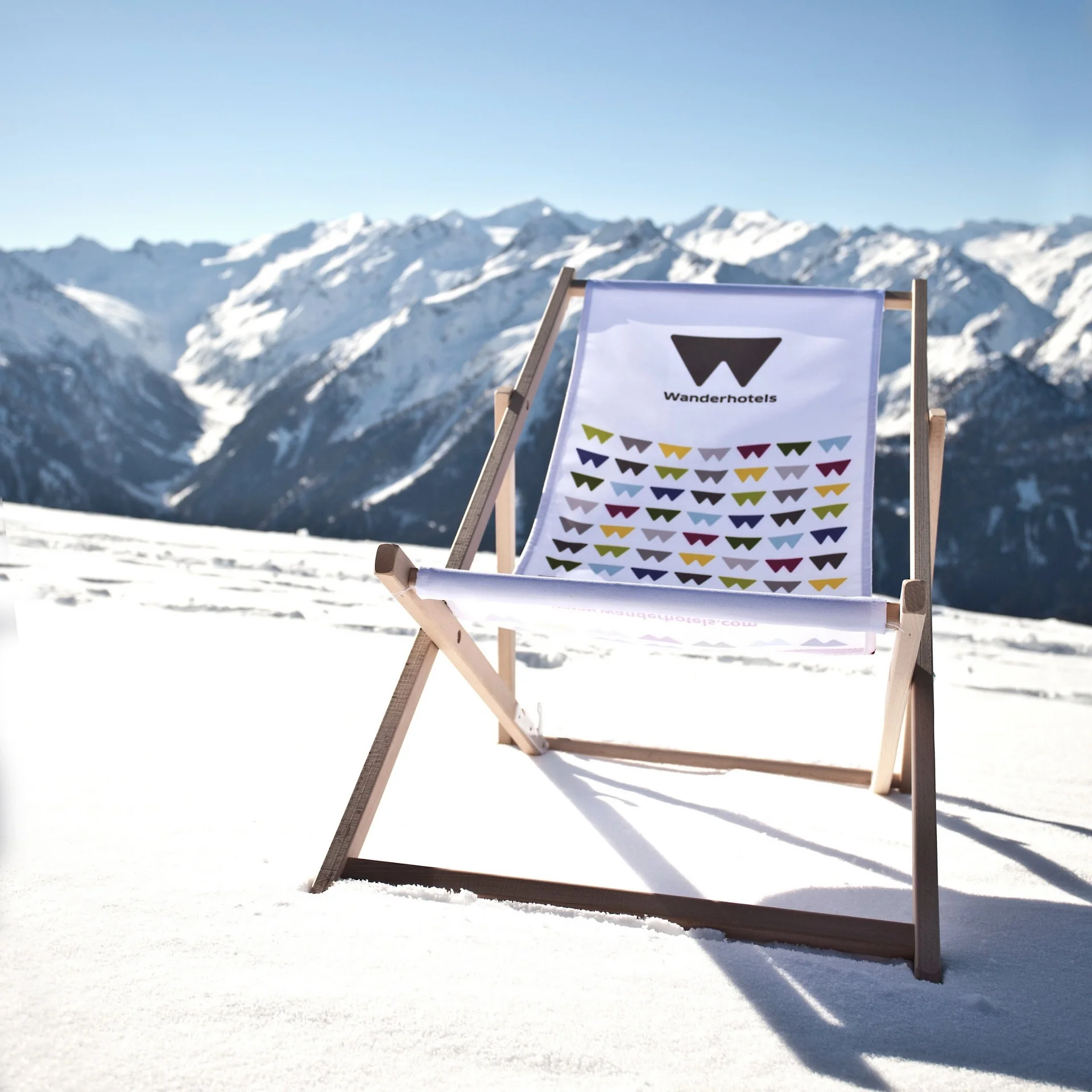 Bewertungen Liegestuhl mit Wanderhotels-Logo auf schneebedecktem Bergpanorama