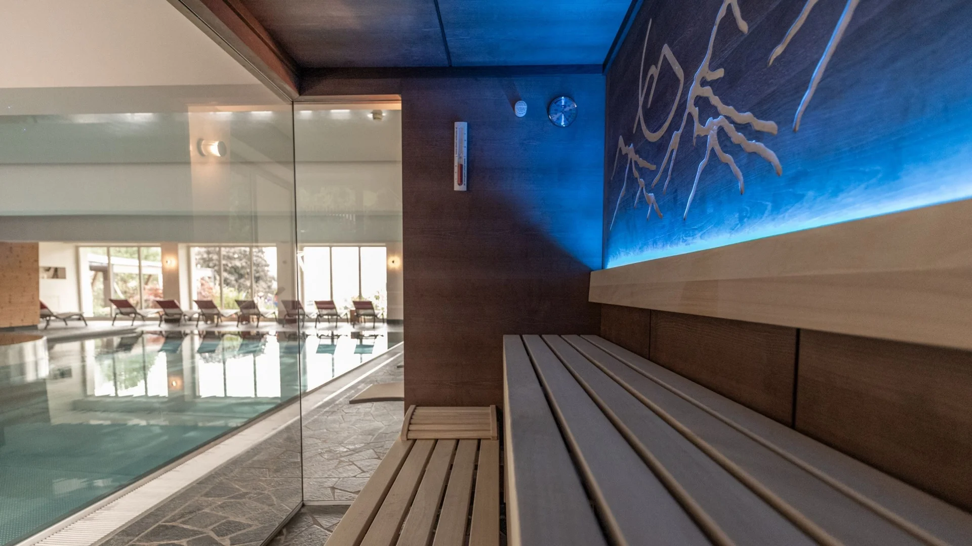 Saunawelt Sauna mit Holzbänken neben einem Innenpool und Liegestühlen im Hintergrund