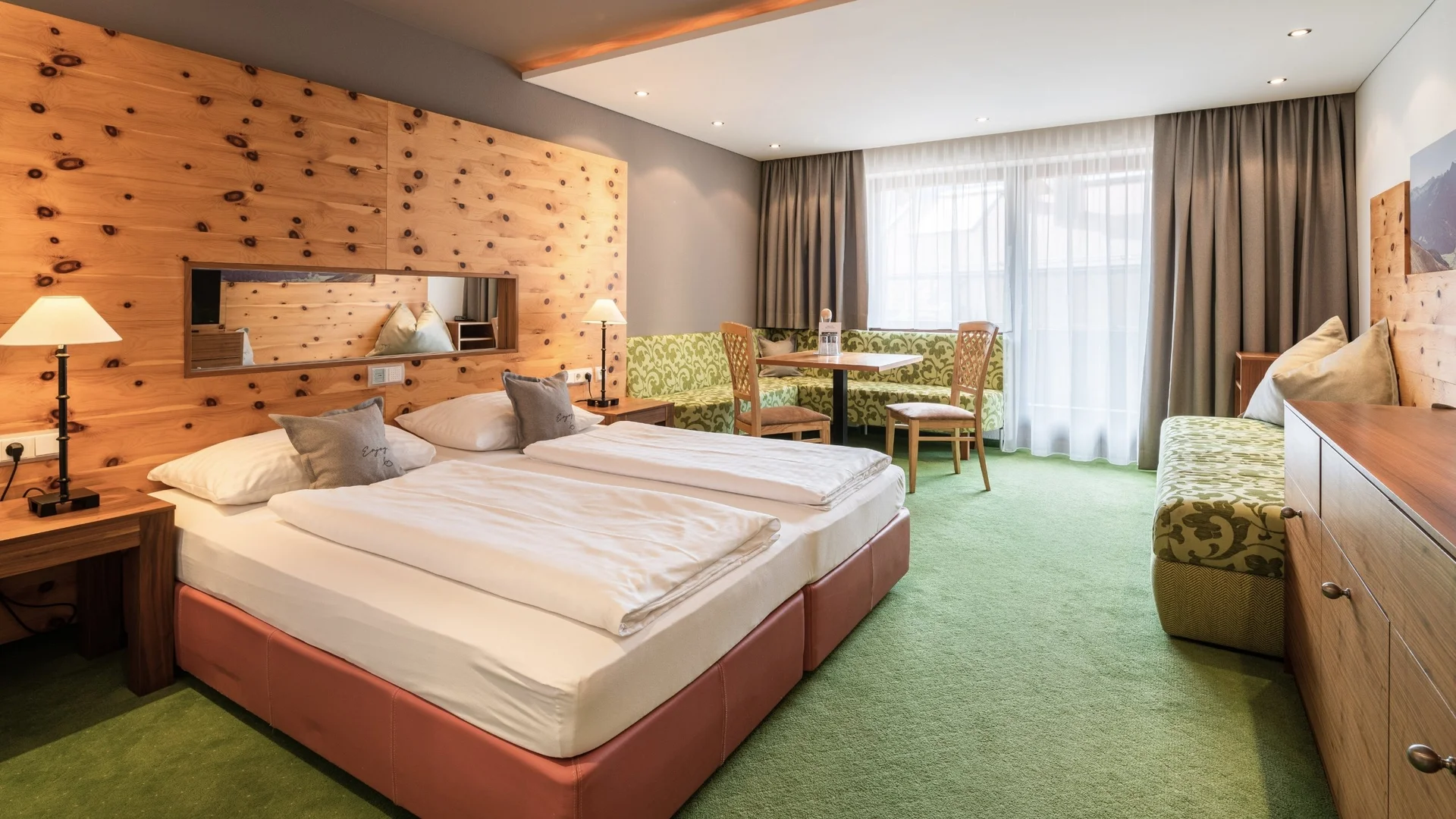 Wohnen Helles Hotelzimmer mit Doppelbett, Holzwand, Sitzecke und grünem Teppich