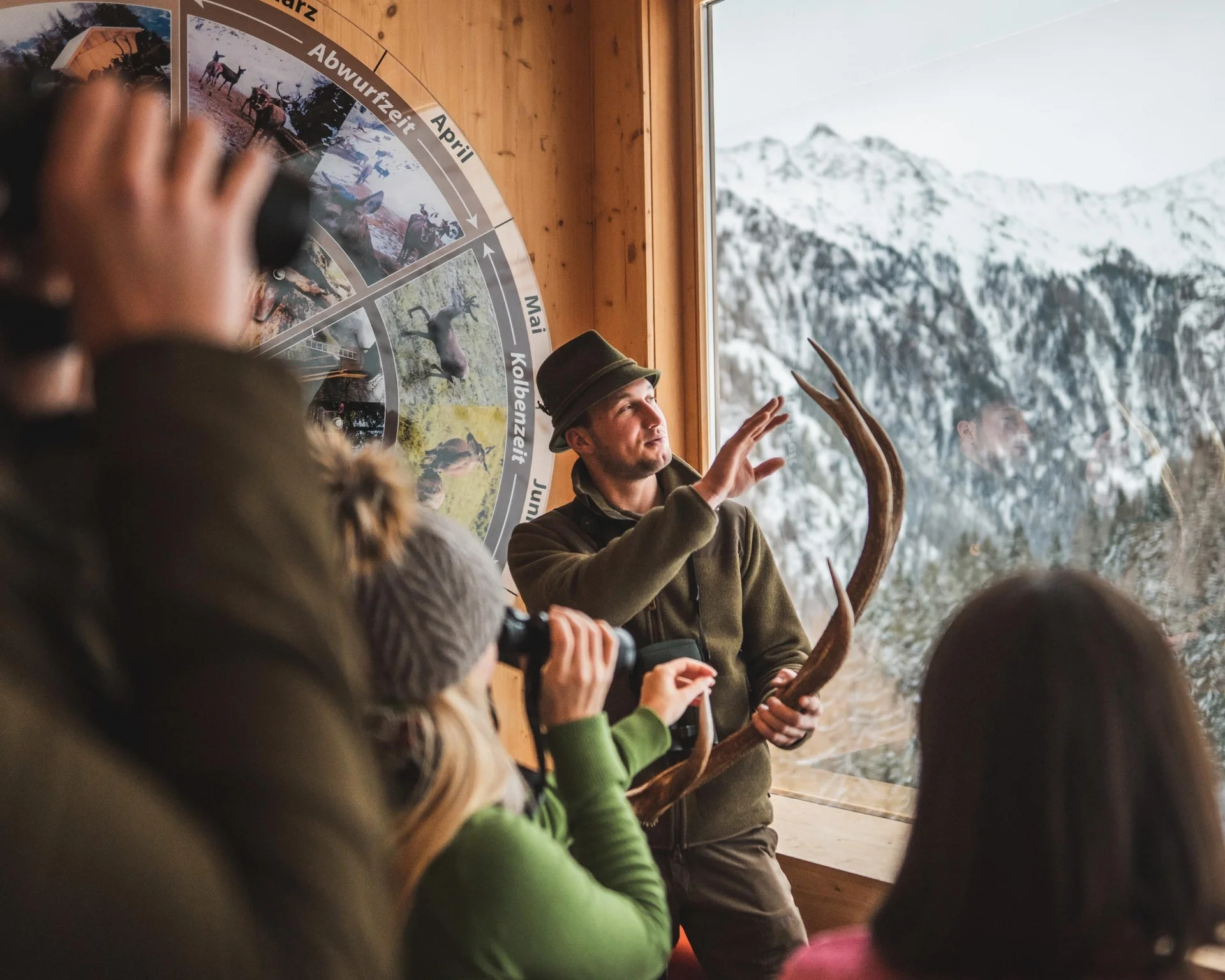 Ausflugstipps Jäger erklärt Besuchergruppe Geweih und Wildtierkalender in Berghütte