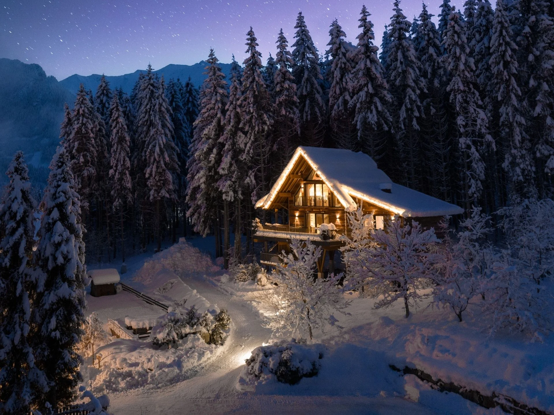 Baumhaus Schneebedecktes Chalet im Wald bei Nacht mit beleuchteten Außenlichtern