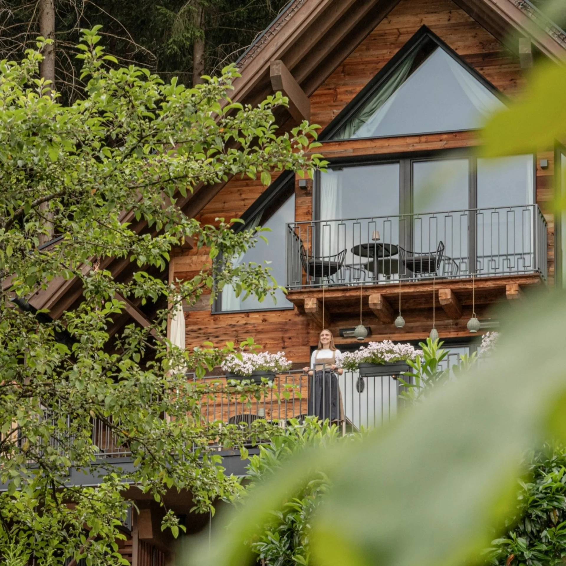 Baumhaus Holzchalet mit Balkon und Frau, umgeben von Bäumen und Pflanzen