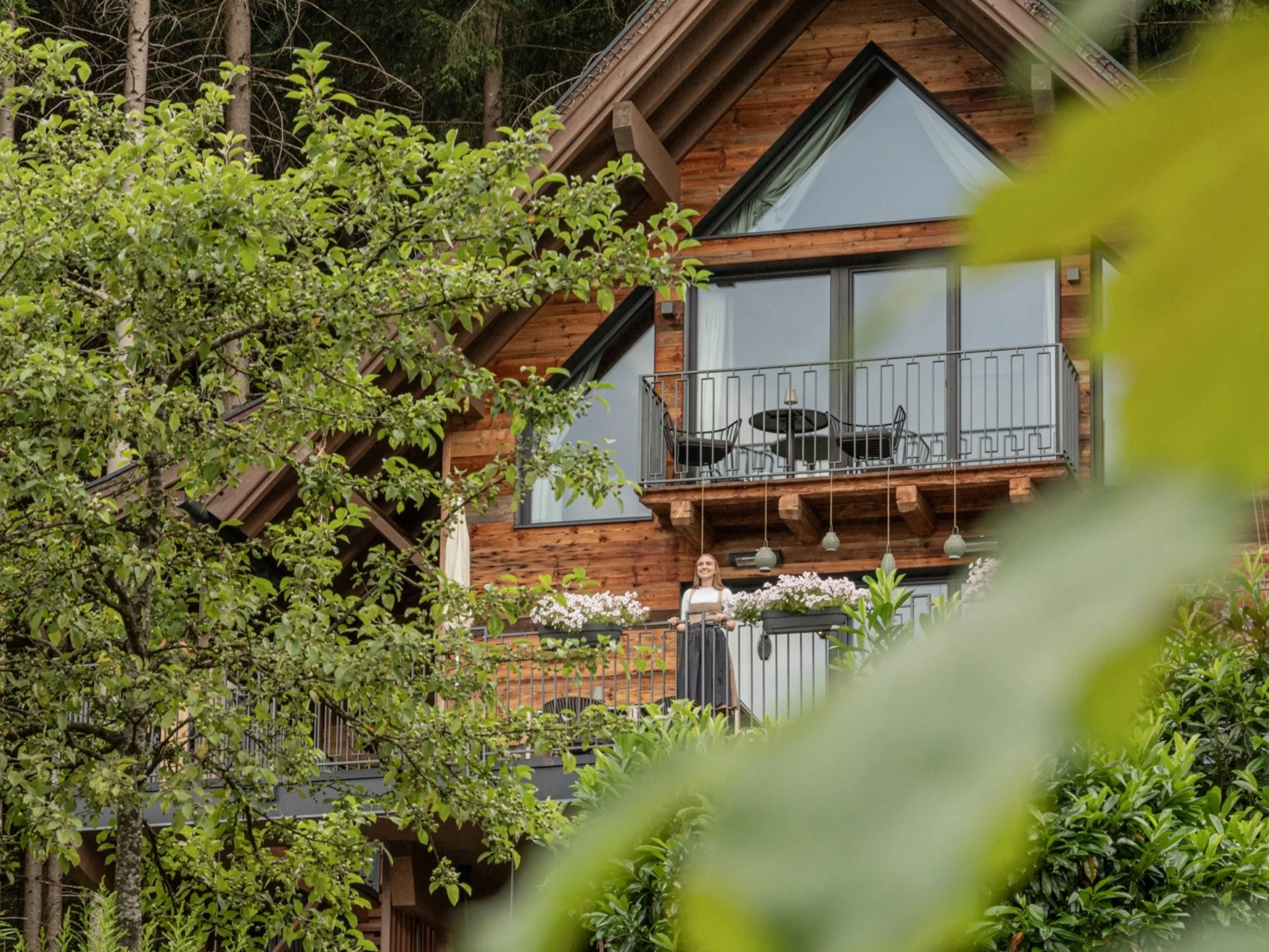 Baumhaus Holzchalet mit Balkon und Frau, umgeben von Bäumen und Pflanzen