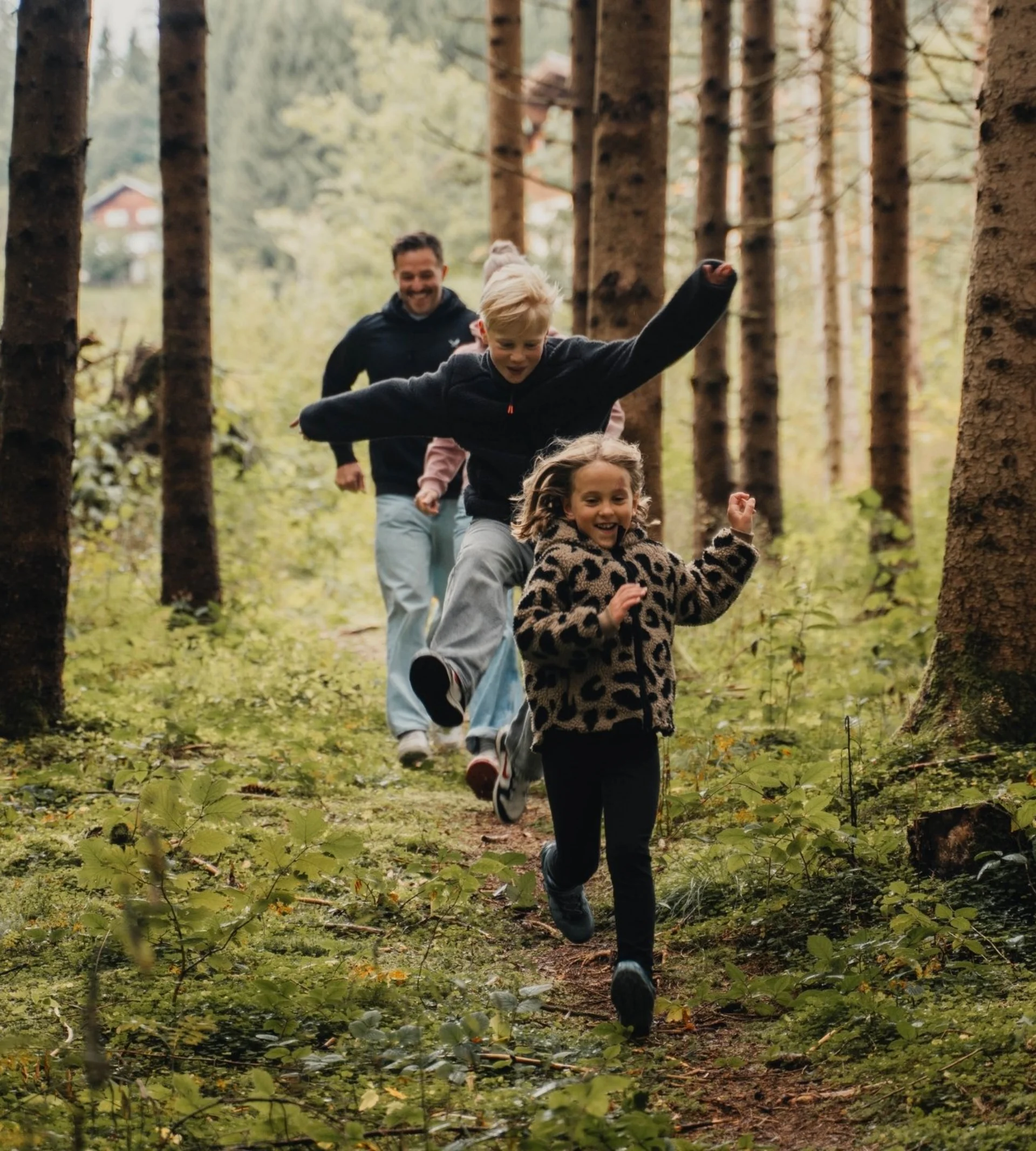 Biken Kinder und Erwachsene laufen fröhlich durch einen Waldweg mit hohen Bäumen