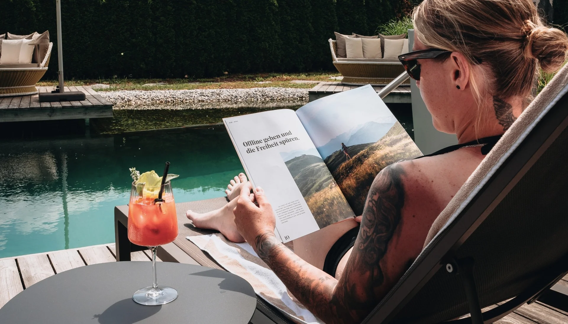 Gassner-Blog Person liest Buch und entspannt am Wasser mit Cocktail auf Tisch