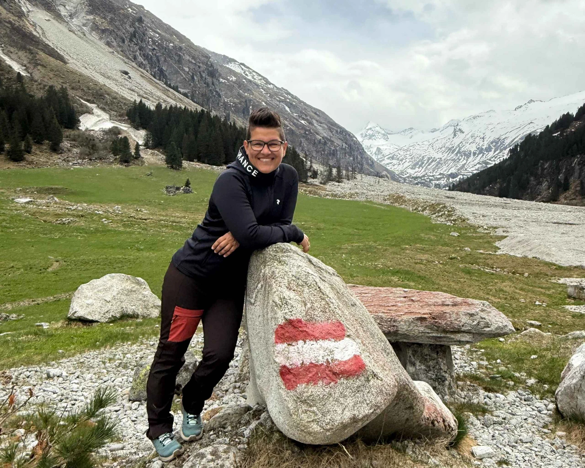 Ausflugstipps Person lehnt an Stein mit rot-weiß-rotem Wanderwegmarkierung in Alpenlandschaft