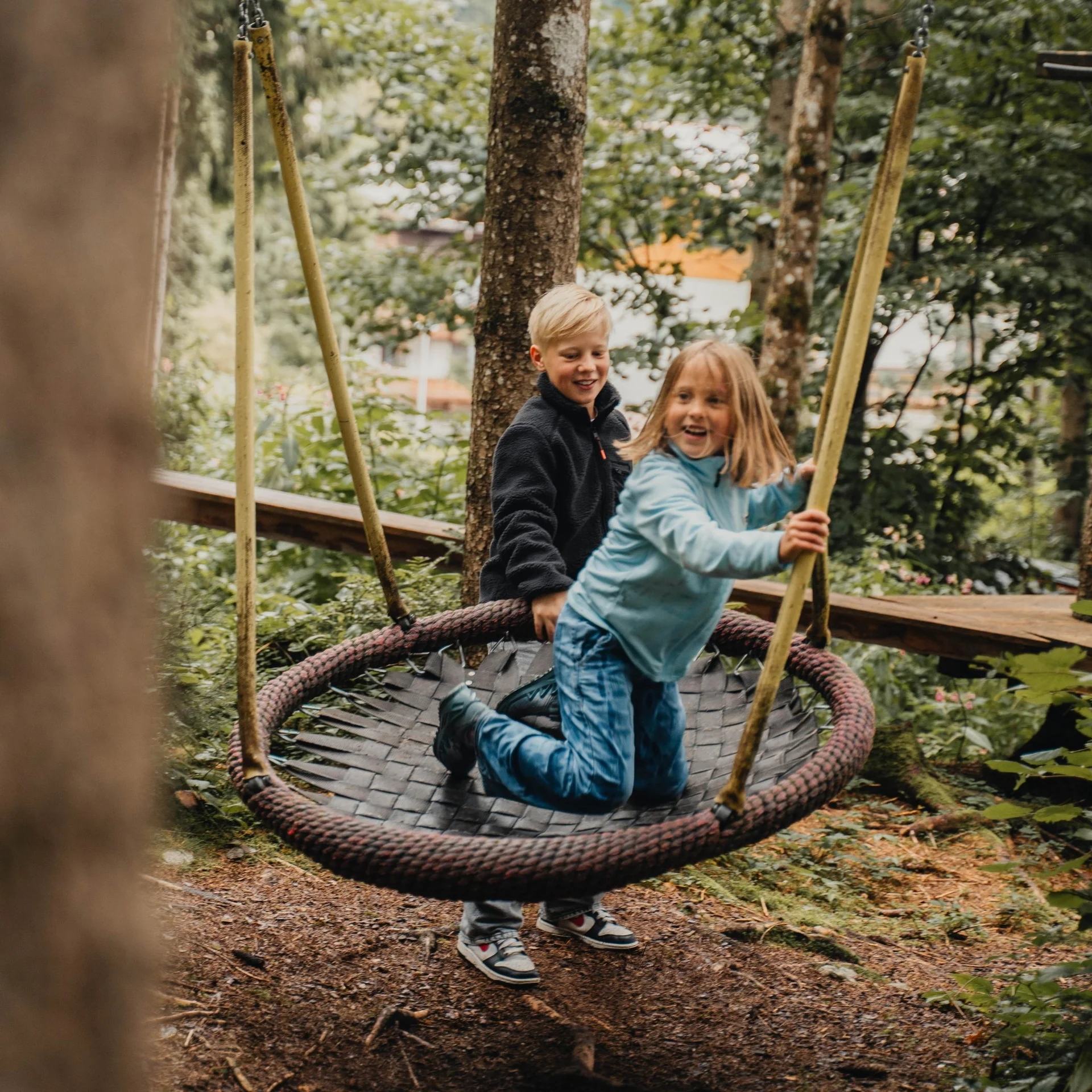 Familienzeit Zwei Kinder spielen auf einem großen Nestschaukel im Wald