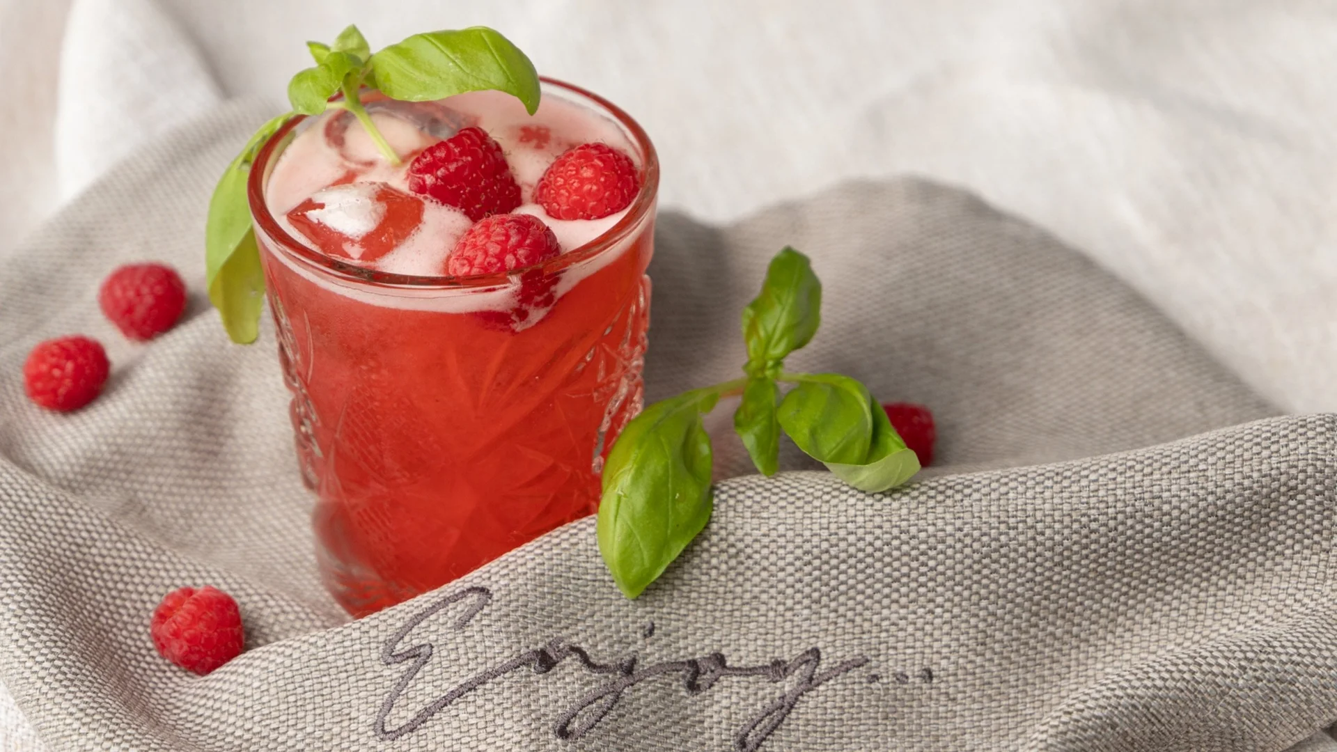 Lehrlingsausbildung Roter Cocktail mit Himbeeren und Basilikum auf grauem Stoff mit Schriftzug Enjoy