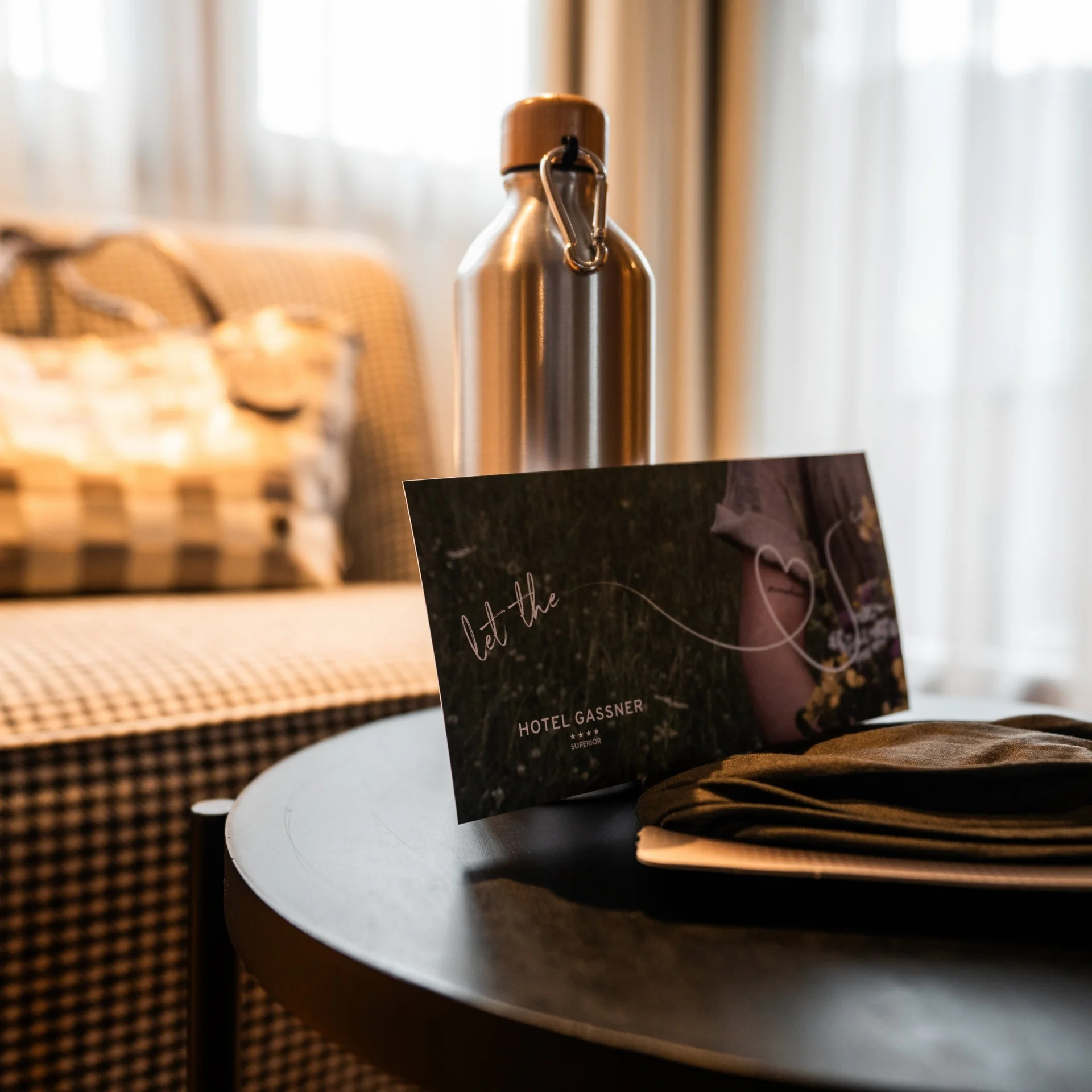 Wohnen Metall-Wasserflasche, Hotelkarte und gefaltetes Tuch auf rundem Tisch in gemütlichem Zimmer