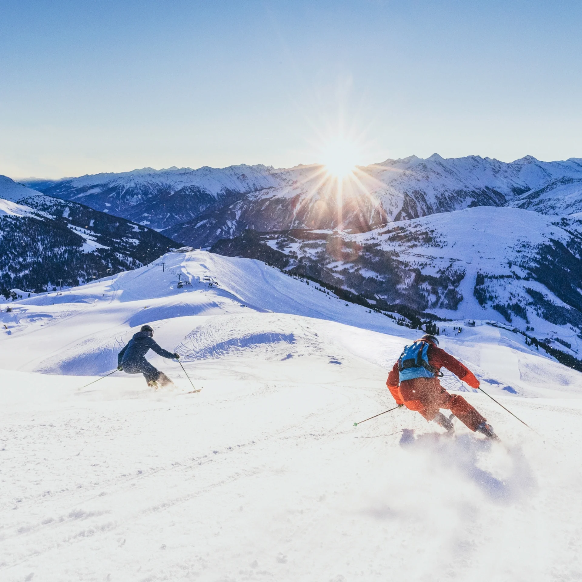 Skifahren Zwei Skifahrer fahren im Sonnenschein einen verschneiten Berg hinunter
